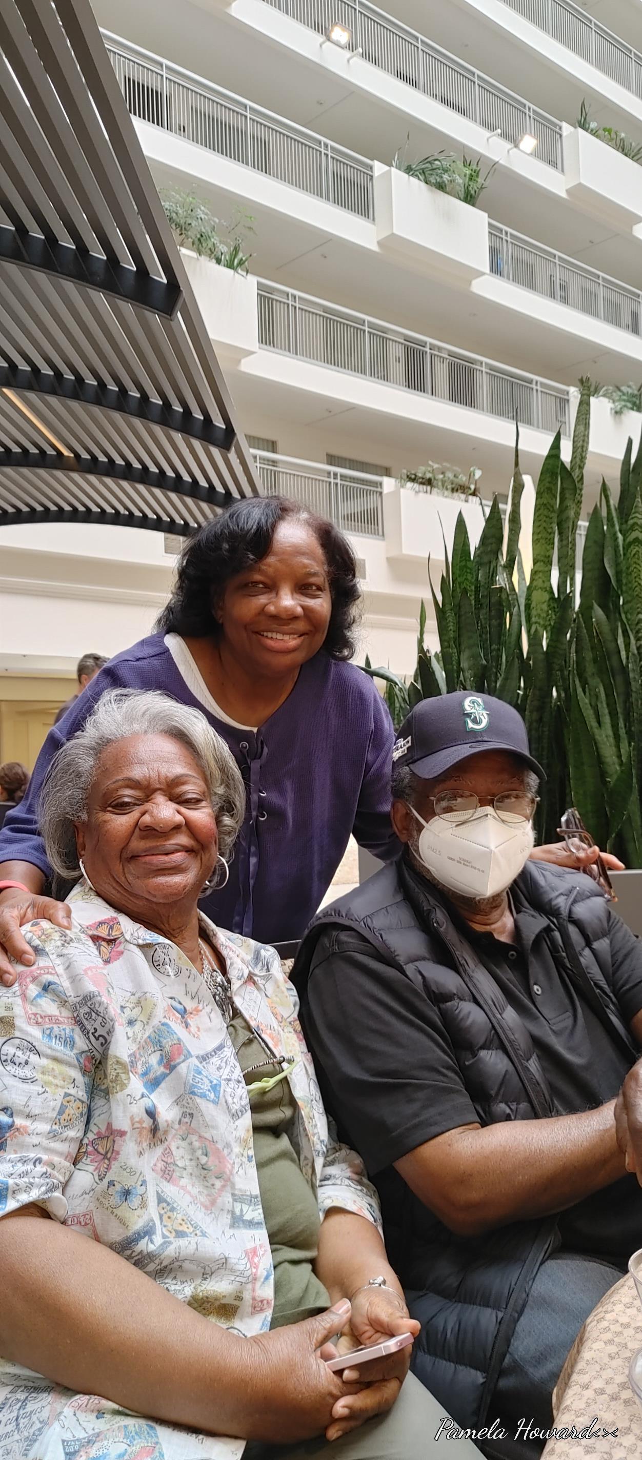 Three family members share a joyful moment indoors, surrounded by plants.