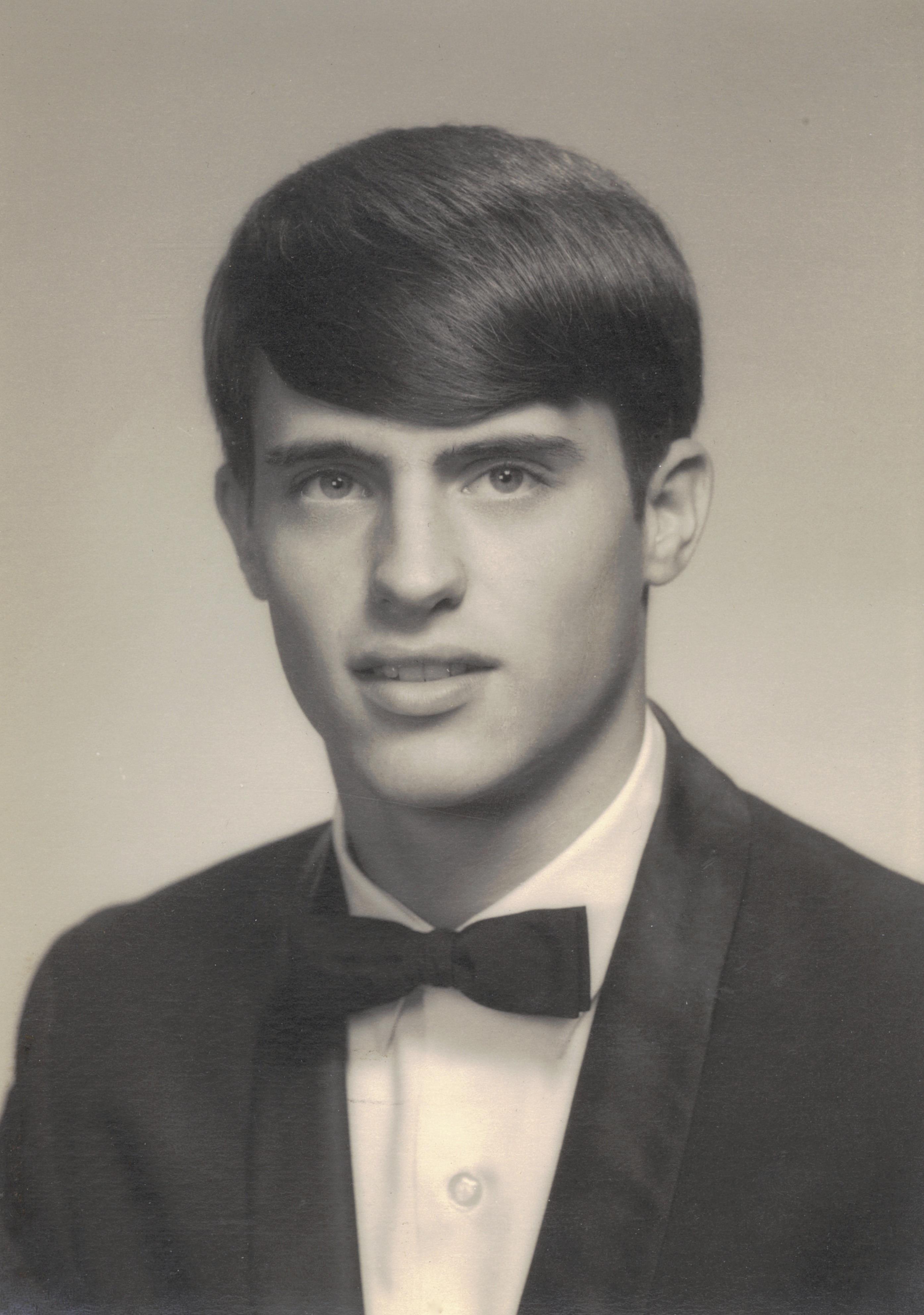 A young man with a well-groomed hairstyle wears a tuxedo with a bow tie, smiling confidently.