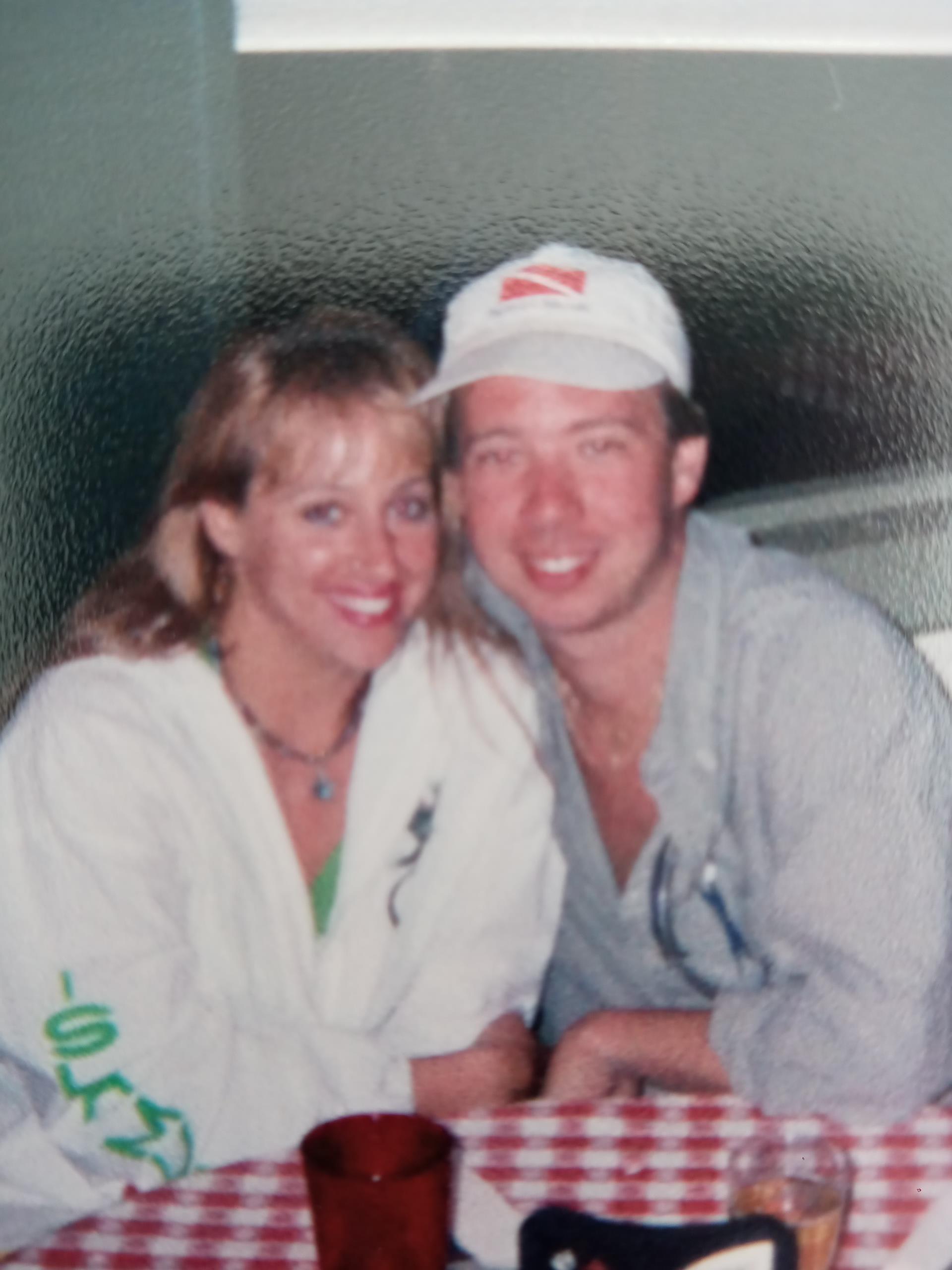 Two people sit closely at a table in a diner, smiling at the camera and enjoying their time.