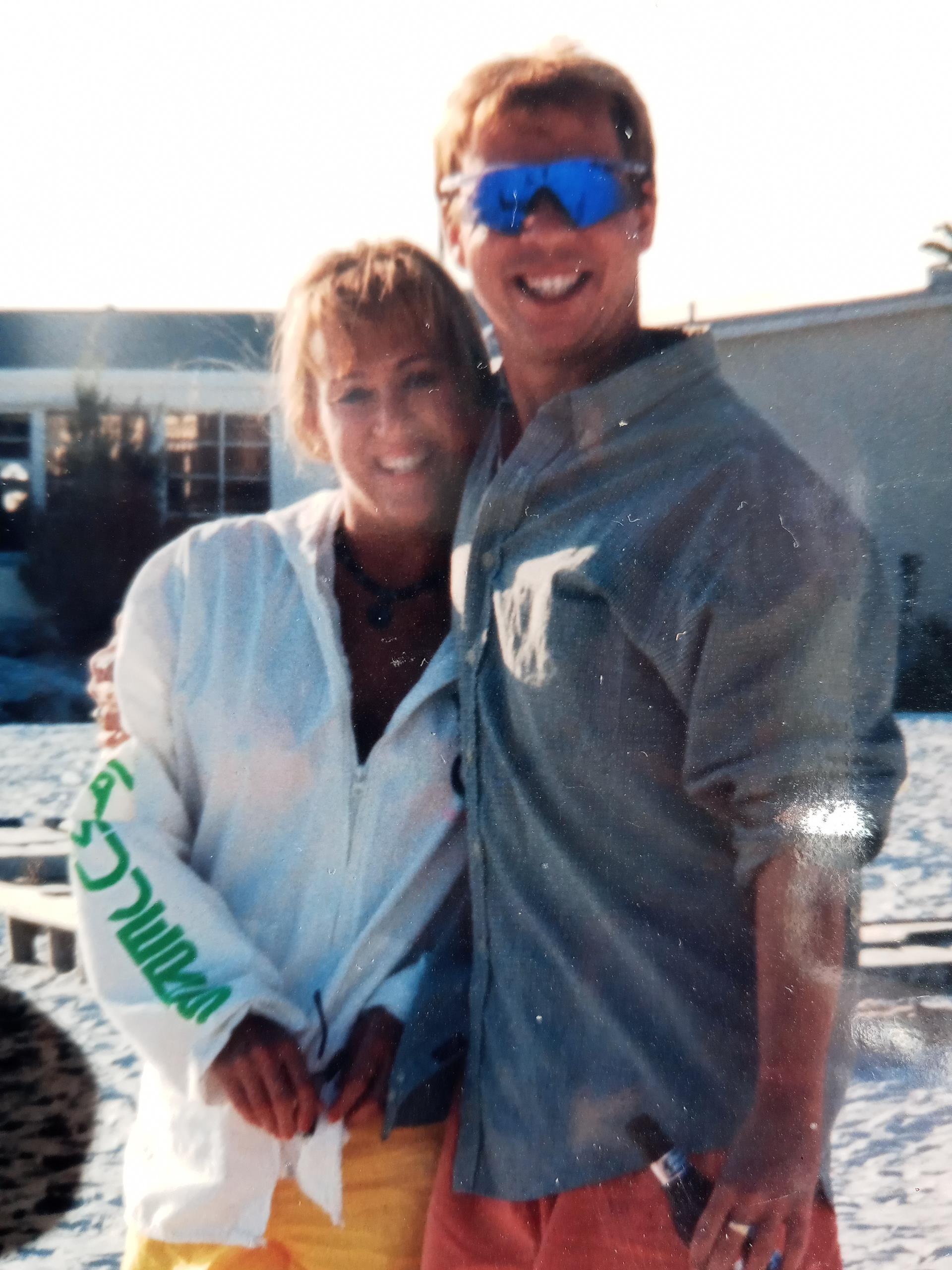 Happy couple stands together on the beach, dressed in summer attire, enjoying their day.