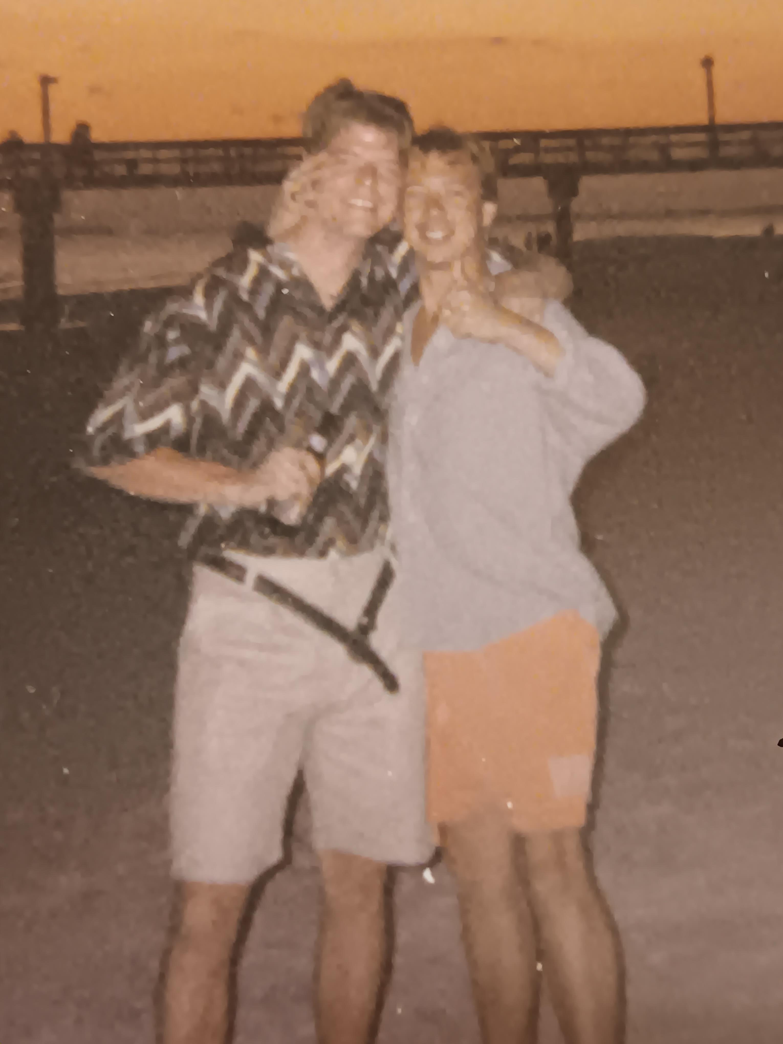 Two friends strike playful poses at the beach during sunset, capturing a joyful memory together.