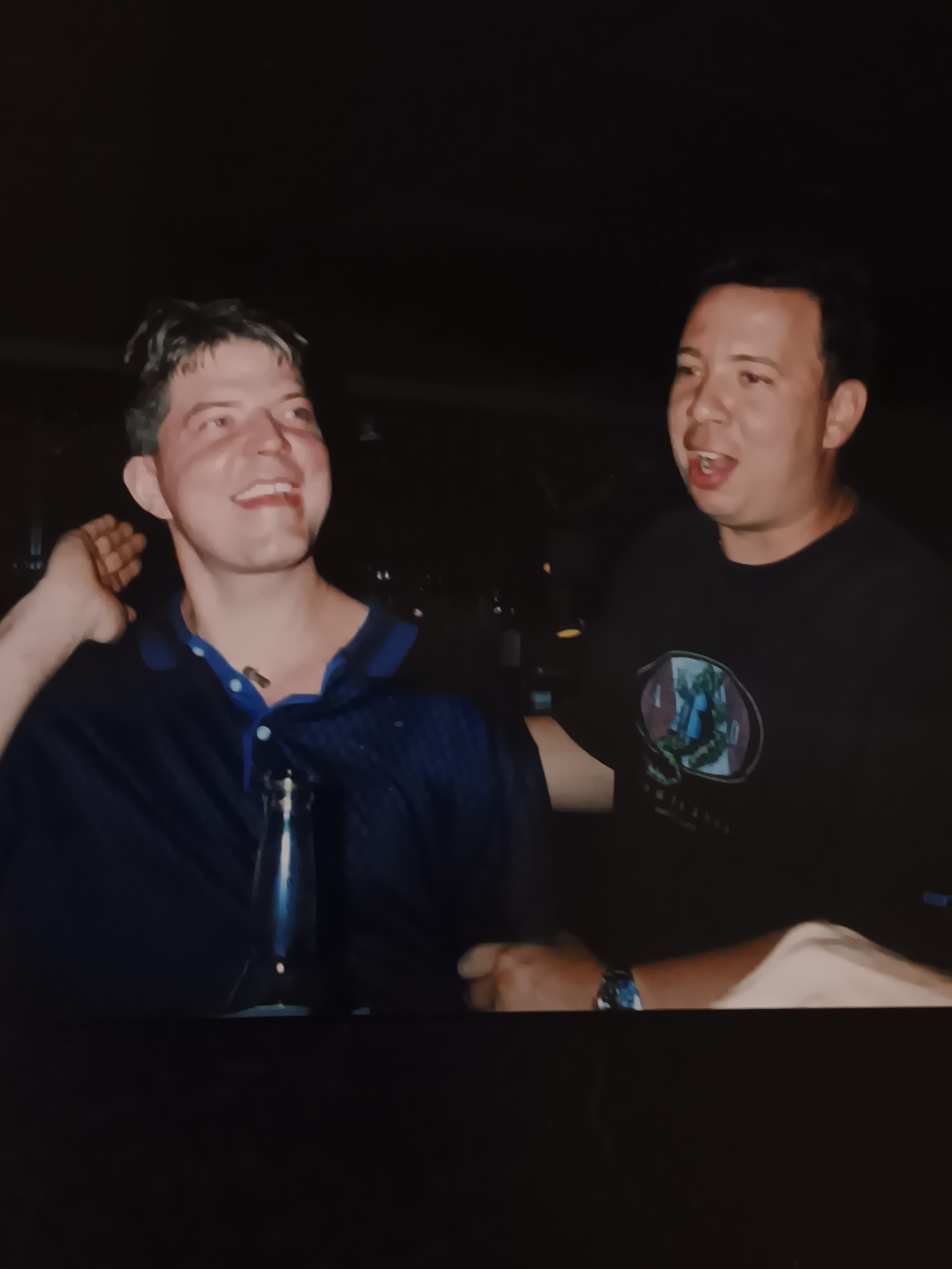 Two men engage in a joyful conversation at a vibrant social event in the evening.