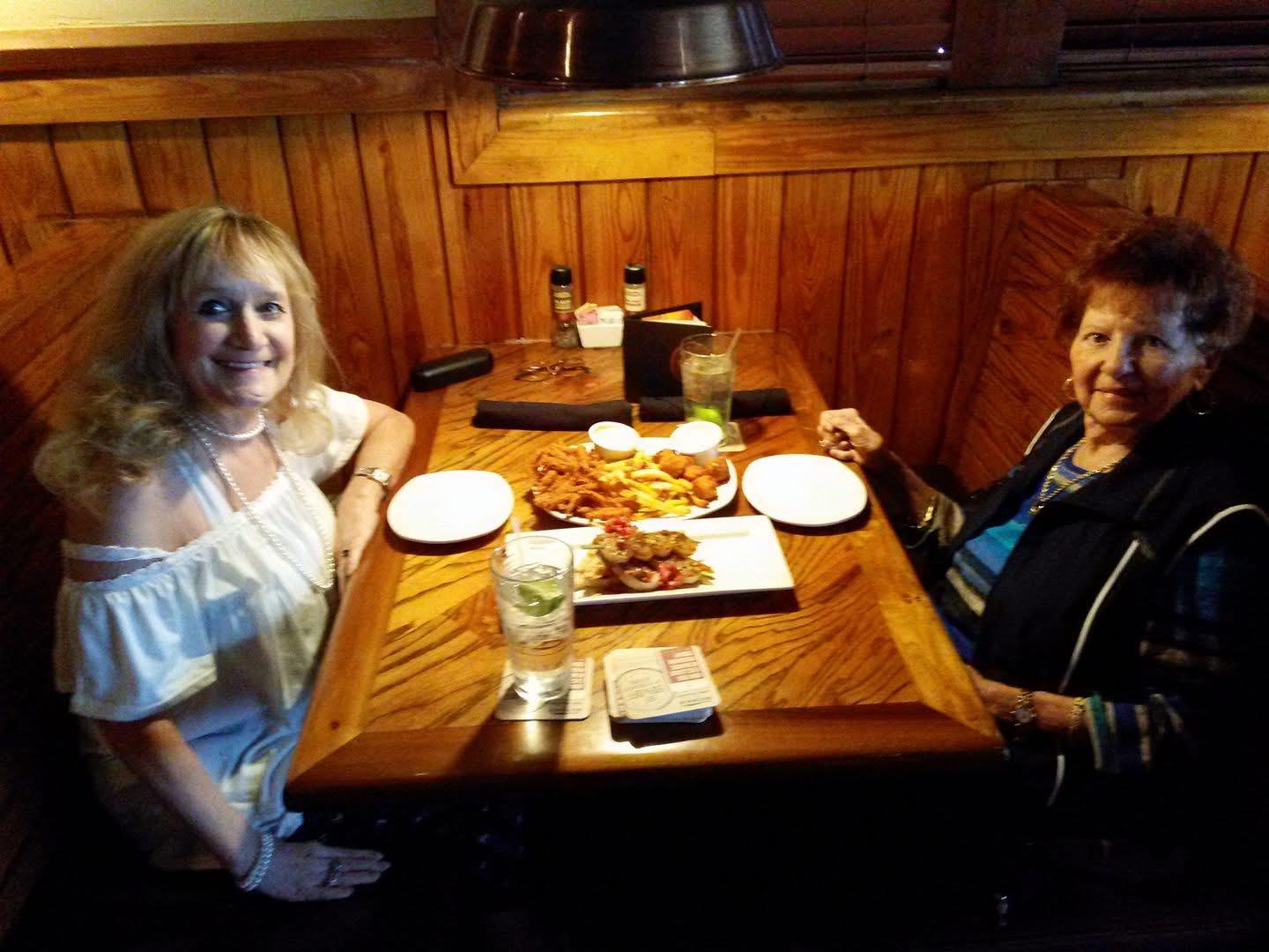 Two women share laughter and food at a wooden table in a restaurant during an afternoon outing.