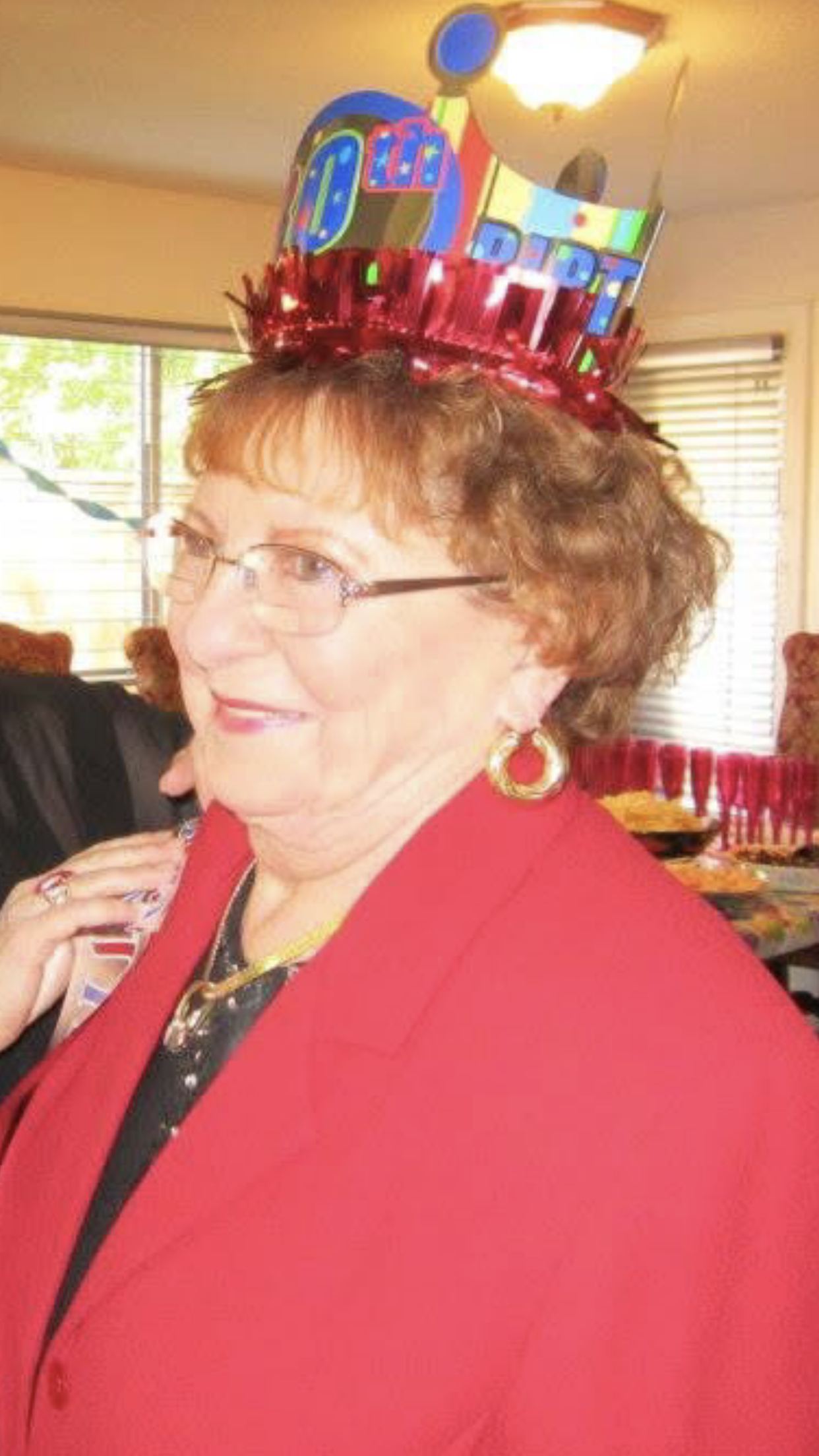 A woman enjoys her special birthday celebration wearing a colorful crown, surrounded by loved ones.