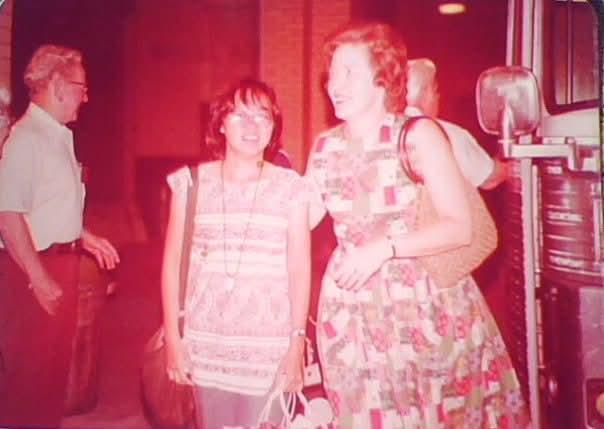 Two women smile while chatting during a community event, with others in the background.