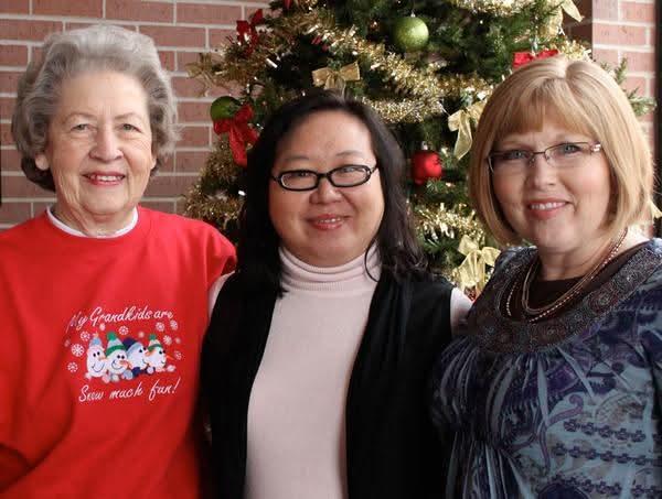 Three women smile and celebrate together near a beautifully decorated Christmas tree in December.