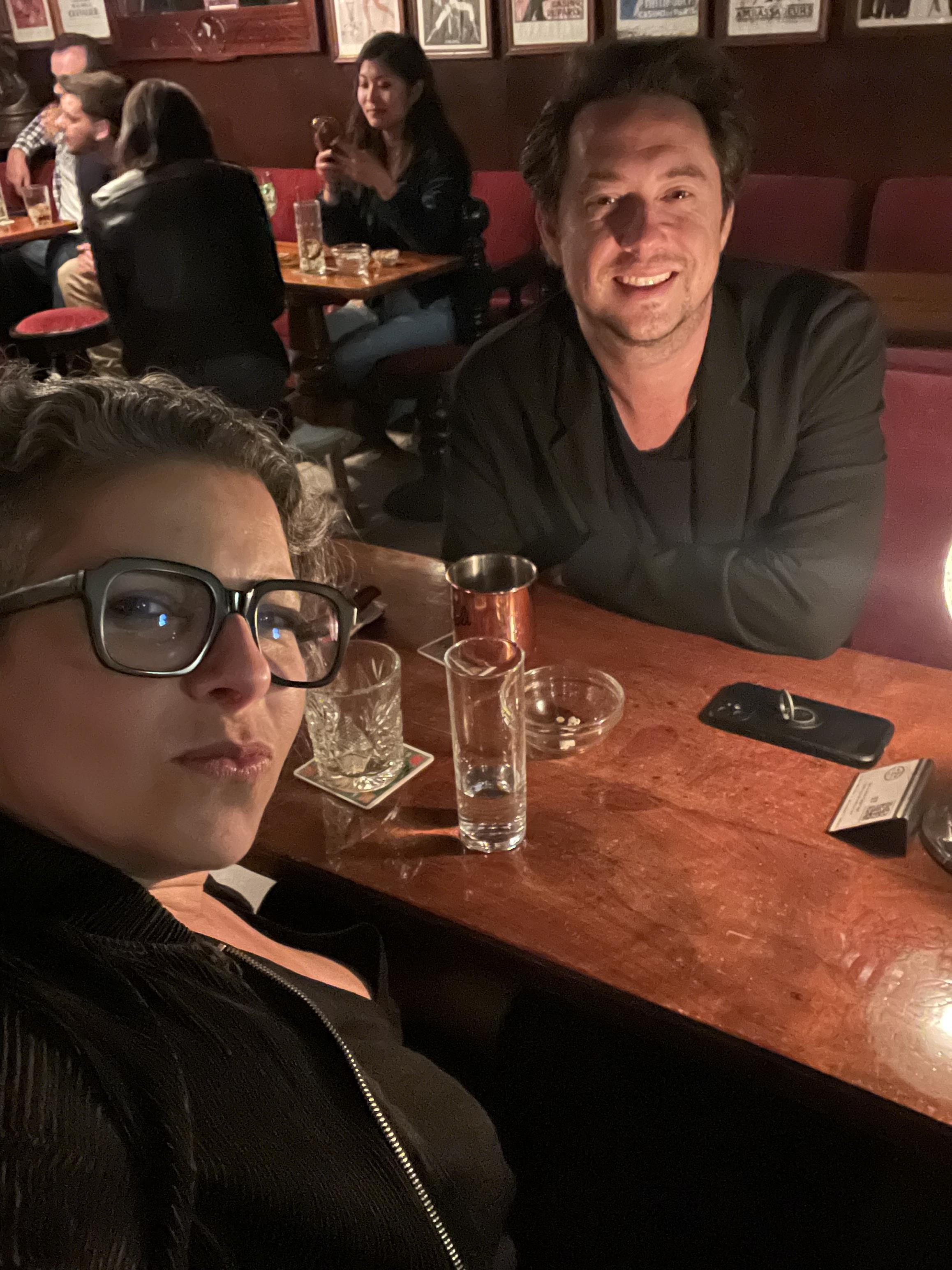 Two friends take a selfie while relaxing at a lively bar, enjoying drinks and conversation.