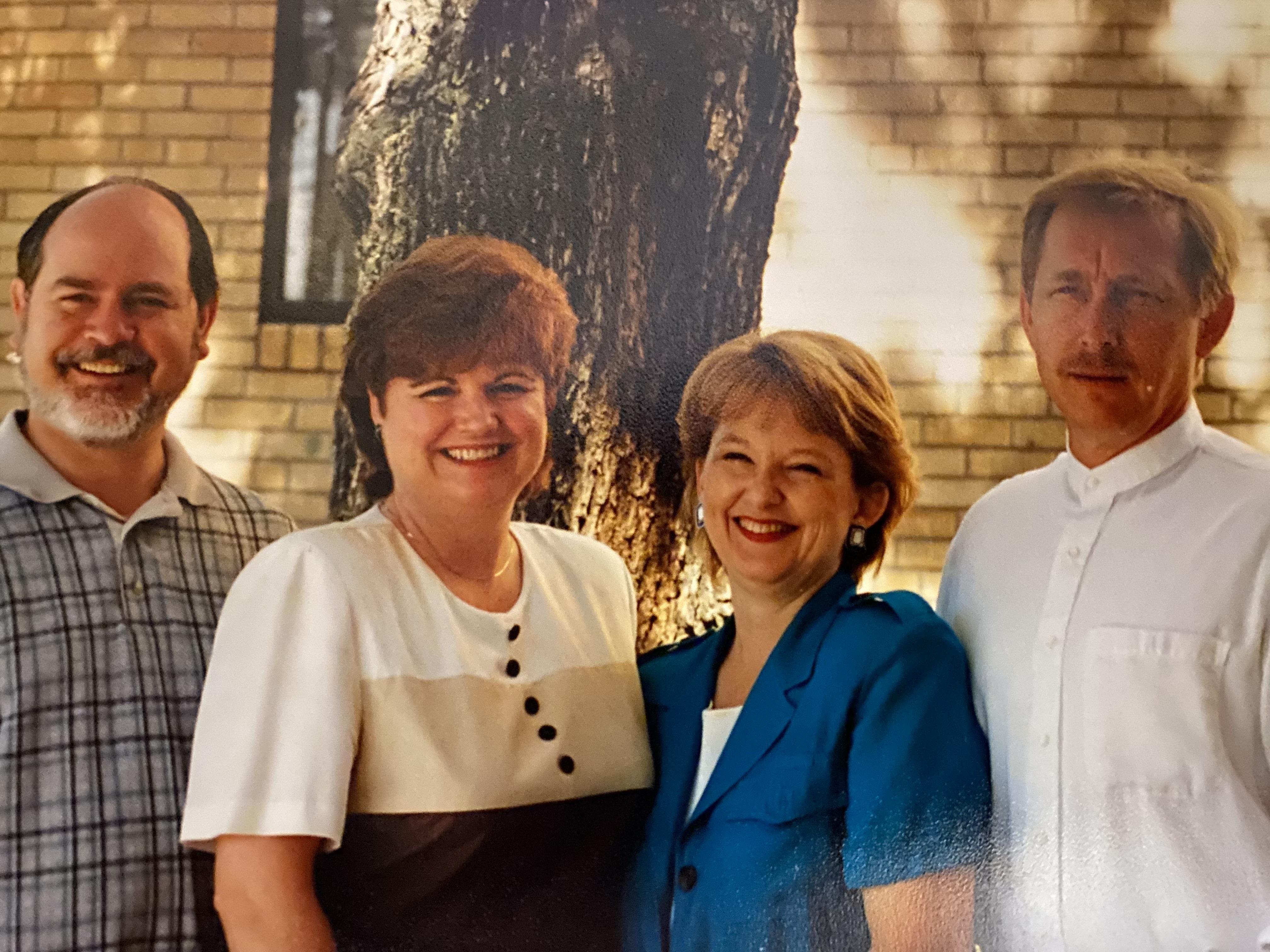 Four friends smile together under a tree, celebrating their reunion in a cheerful atmosphere.
