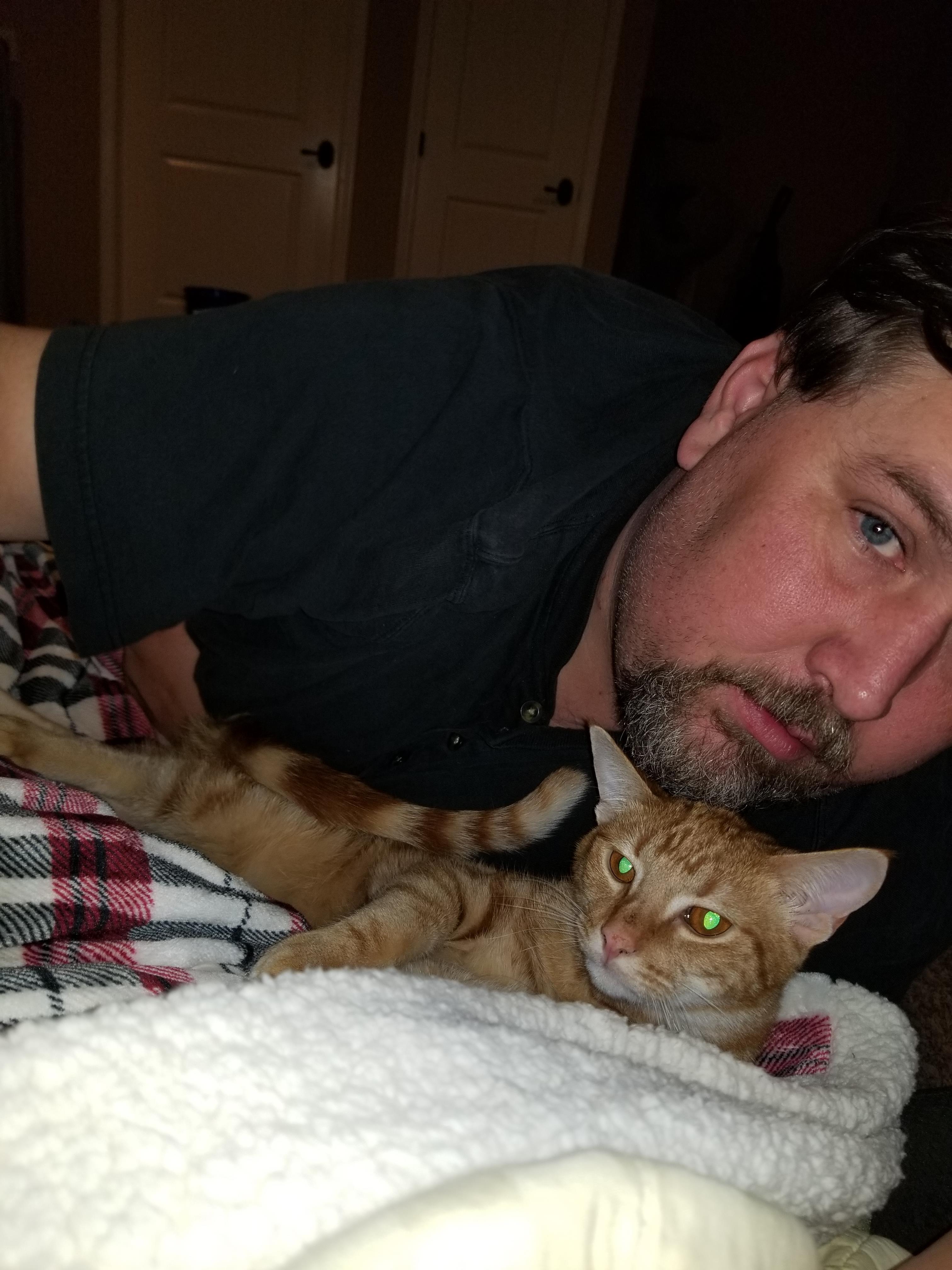 A man relaxes at home with his orange cat nestled beside him, creating a warm atmosphere.