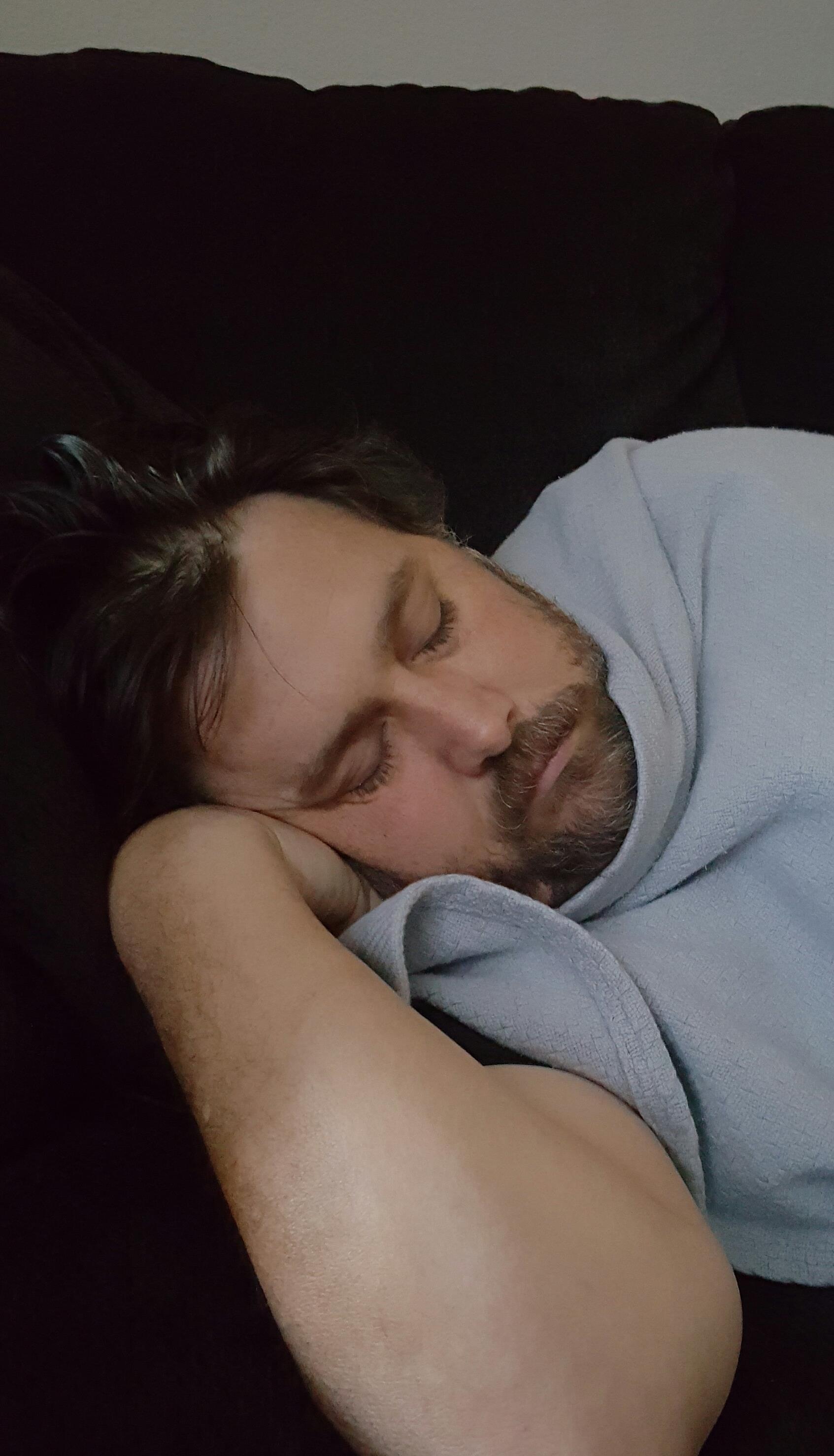 A man is peacefully sleeping on a couch, wrapped in a soft blanket, appearing relaxed and serene.