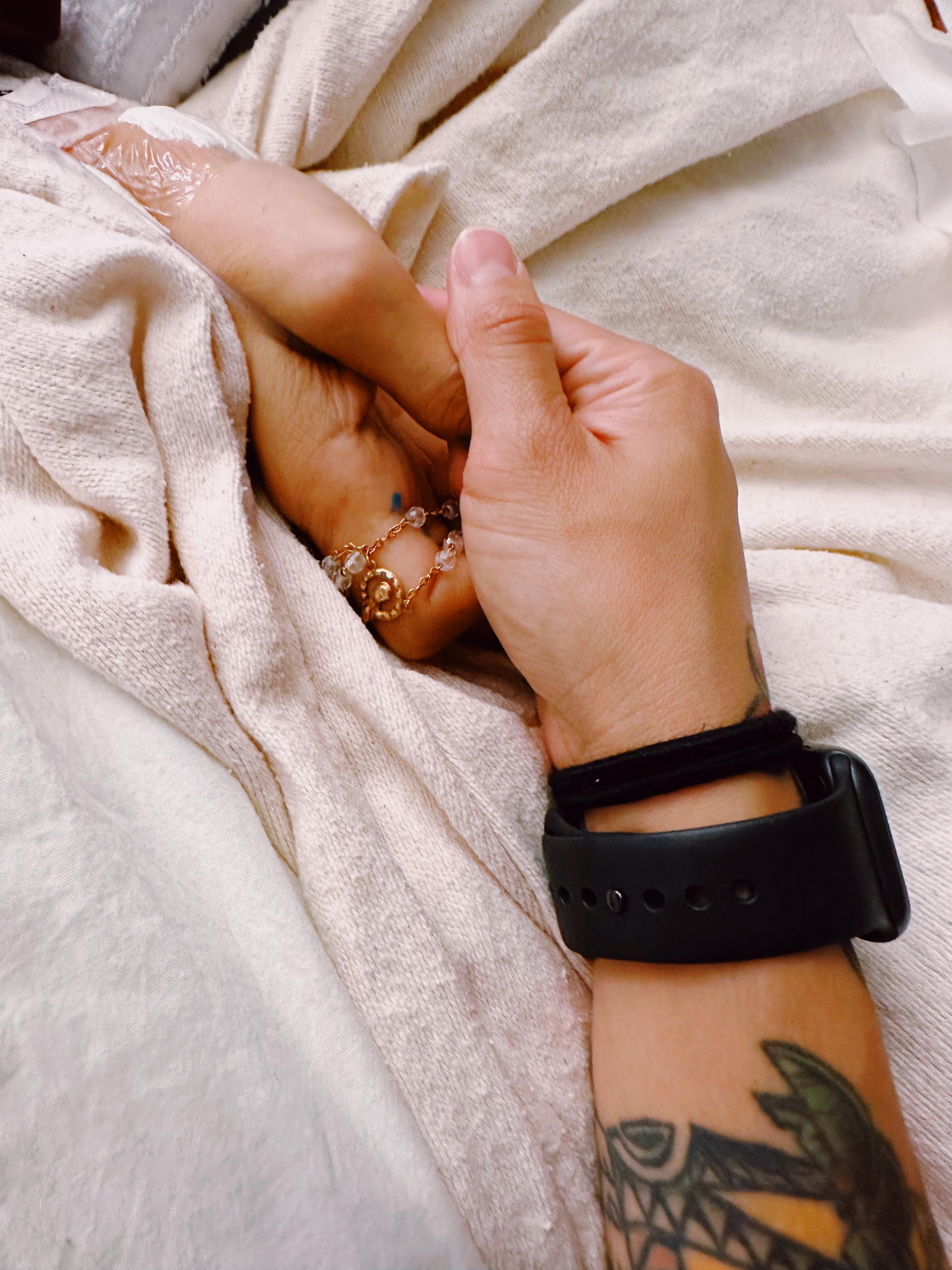 Two hands are intertwined, showcasing jewelry and intricate henna designs in a warm setting.