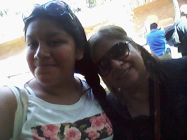 Two individuals smile at the camera while enjoying time with family on a sunny day outdoors.