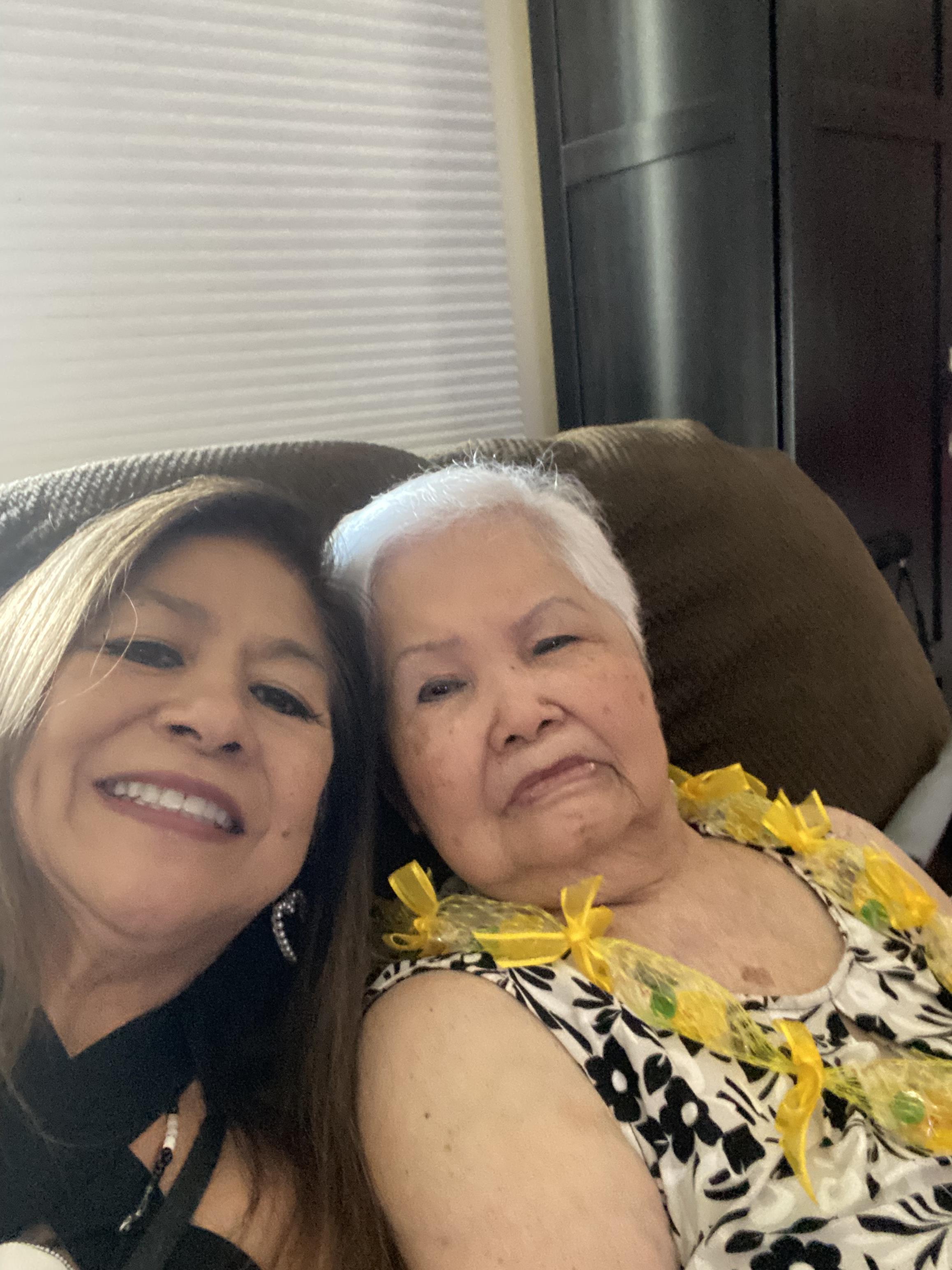 Two family members are smiling together while sitting on a couch, celebrating their bond with leis.