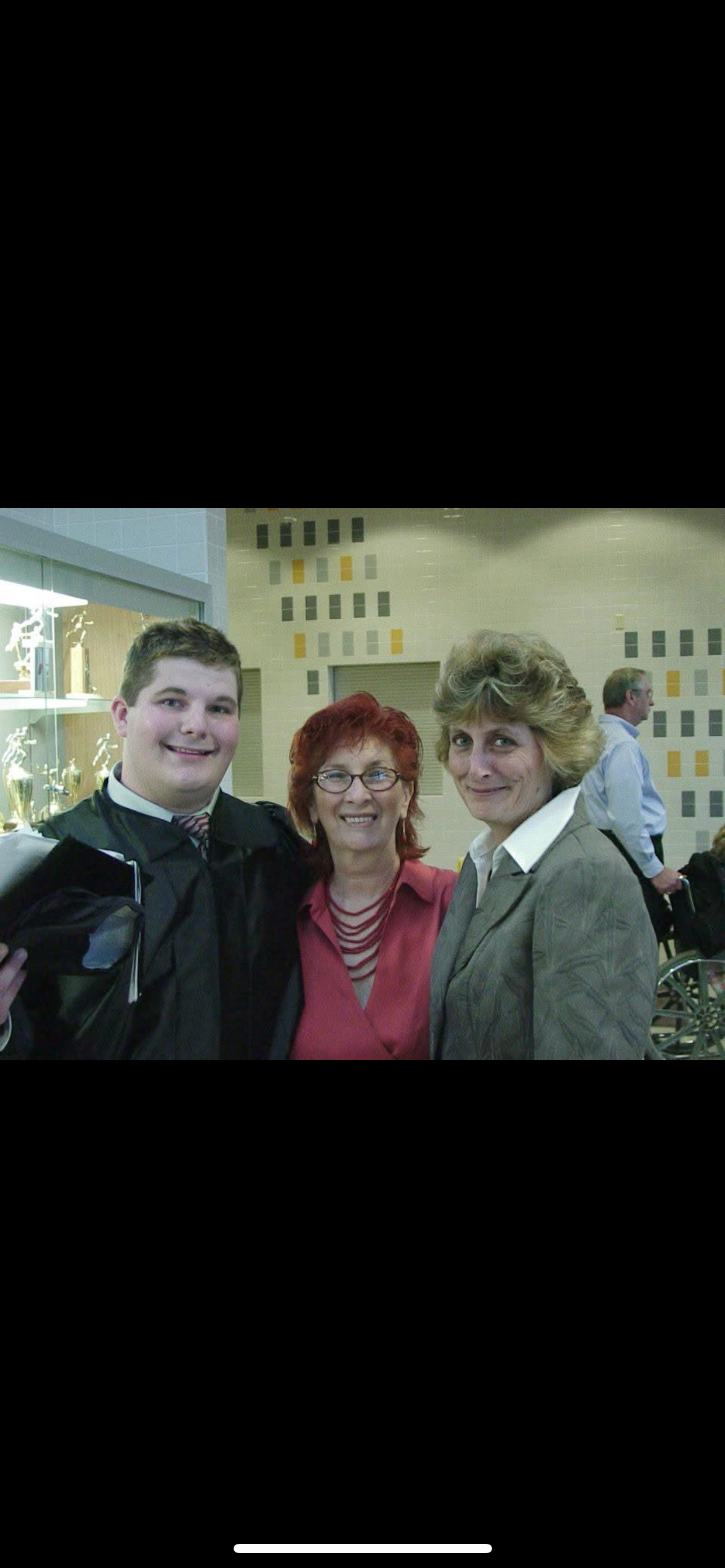 A young graduate smiles proudly with two family members in a school setting.