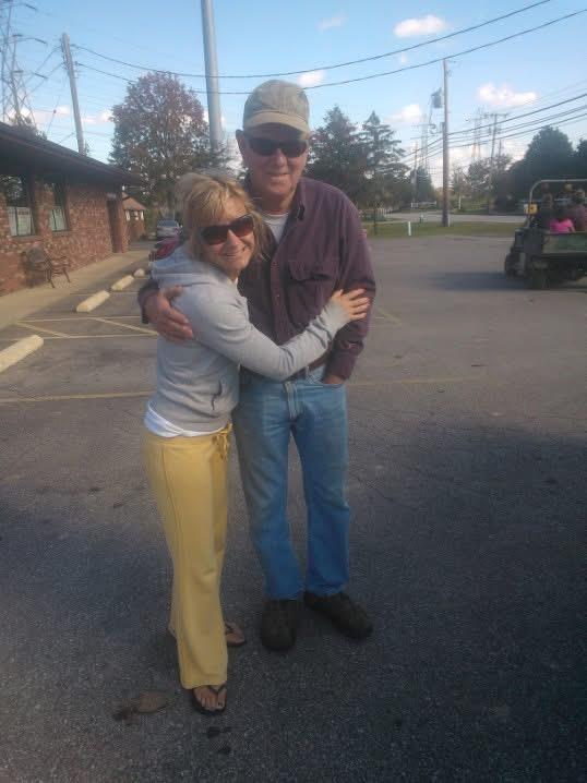 Two friends share a warm hug on a sunny afternoon in a parking area during a casual gathering.