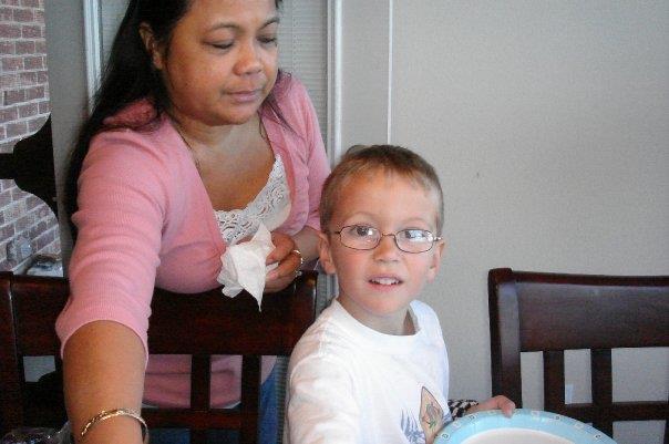 A mother serves food while her young son smiles at the table, celebrating family time together.