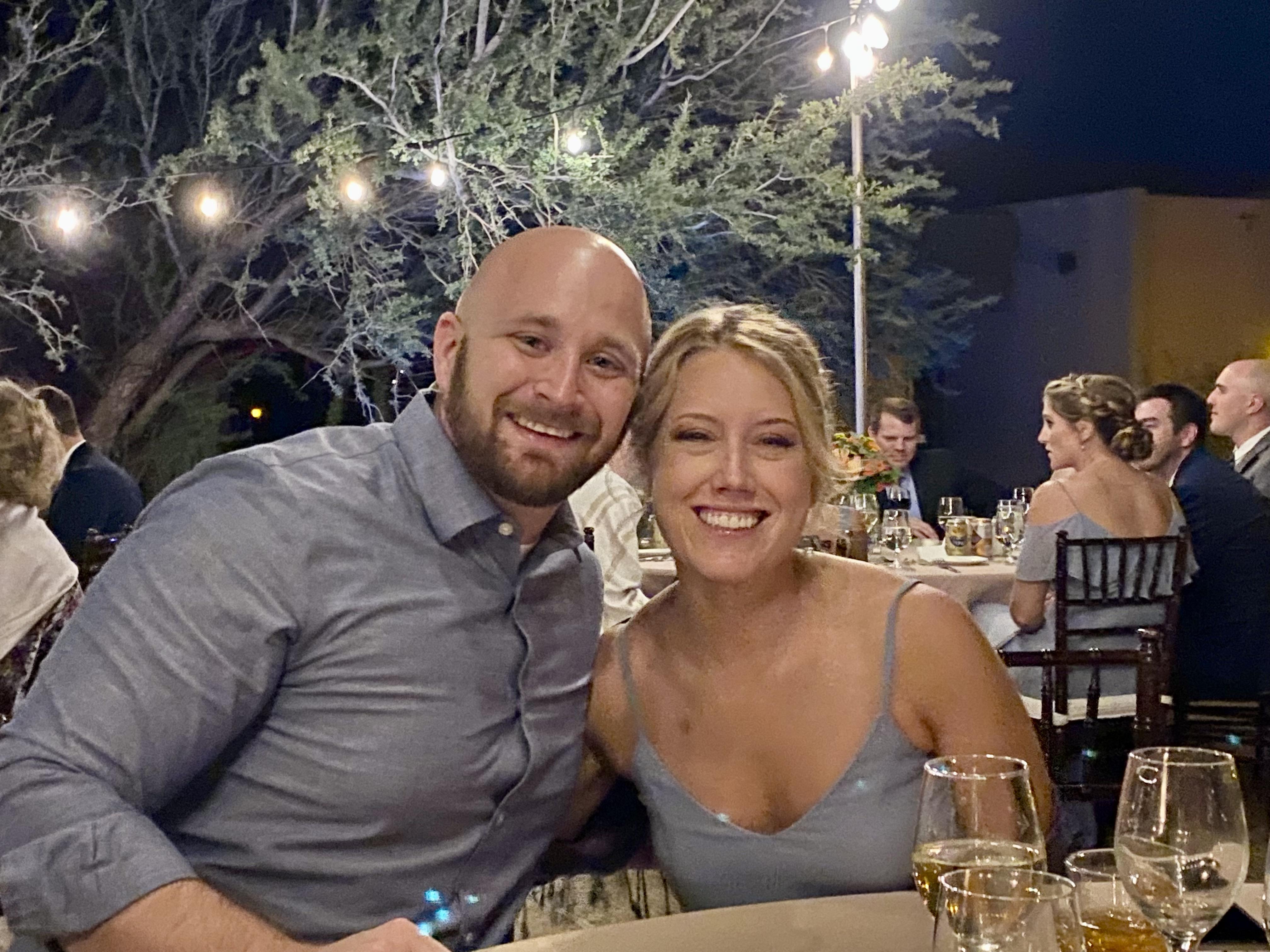 A couple enjoys each other's company at a lively outdoor event under string lights with friends.