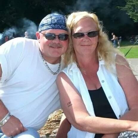 A couple relaxes and smiles at a park, enjoying a sunny day and each other's company.