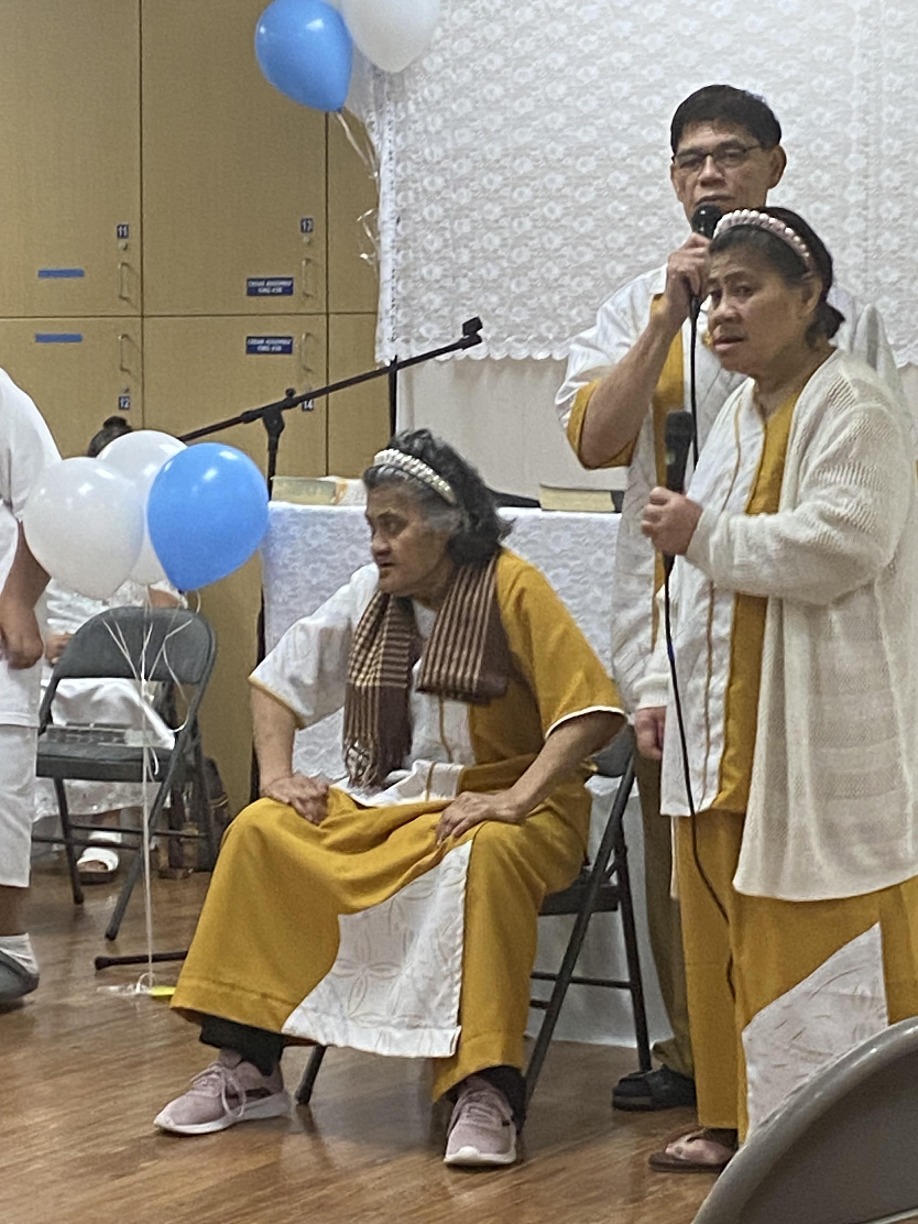 Two seniors sing a traditional song as another engages the audience with speaking.