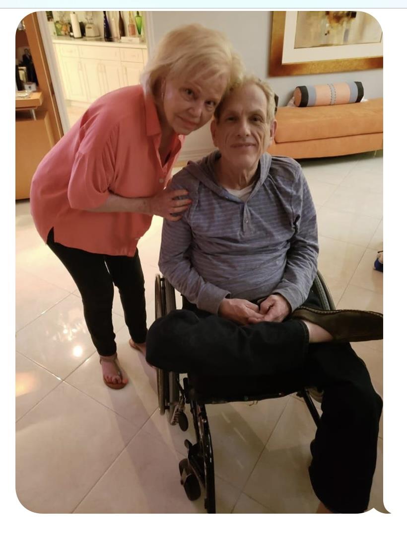 A woman leans affectionately beside a man in a wheelchair while they share a moment.