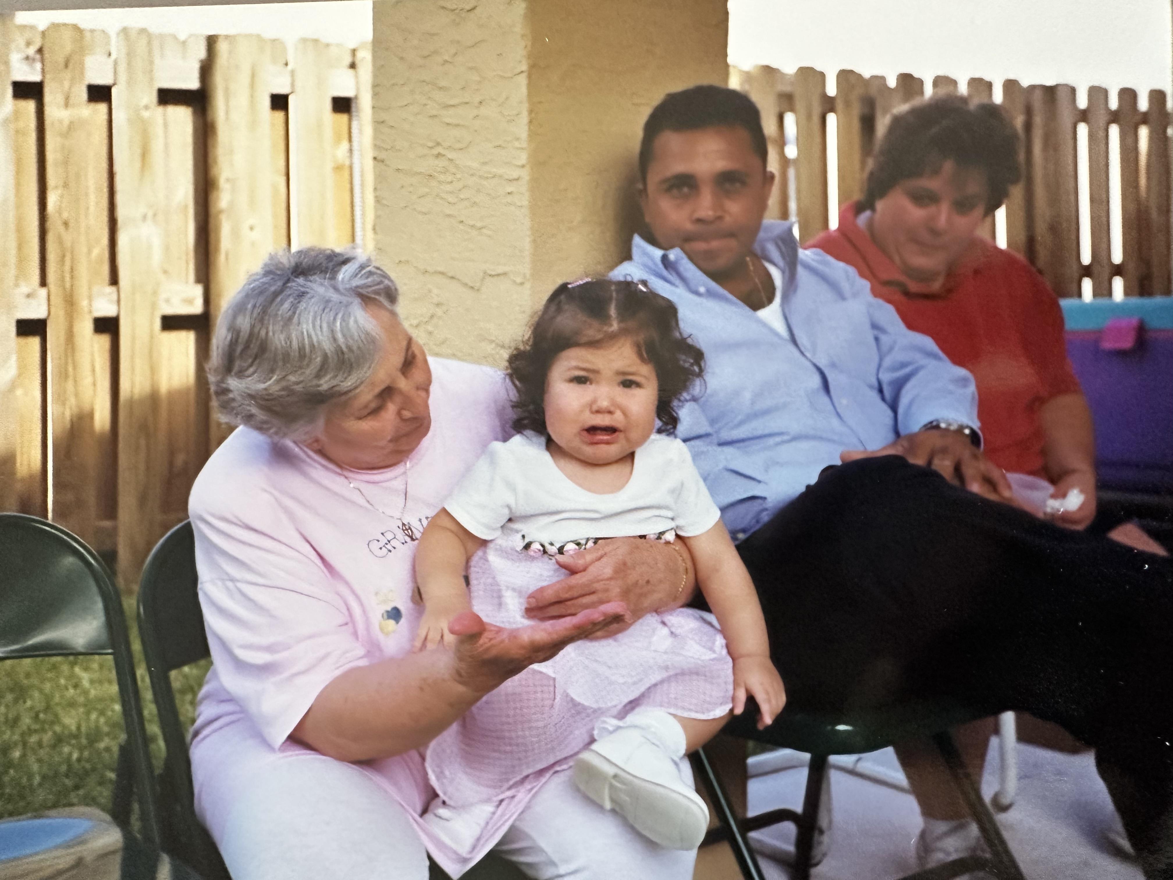 A group of family members sits together enjoying a warm, sunny day in the backyard.