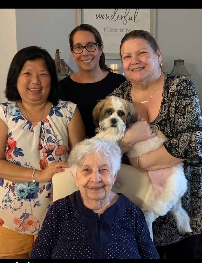 Four generations of women share smiles and joy while holding a small dog in a cozy home.