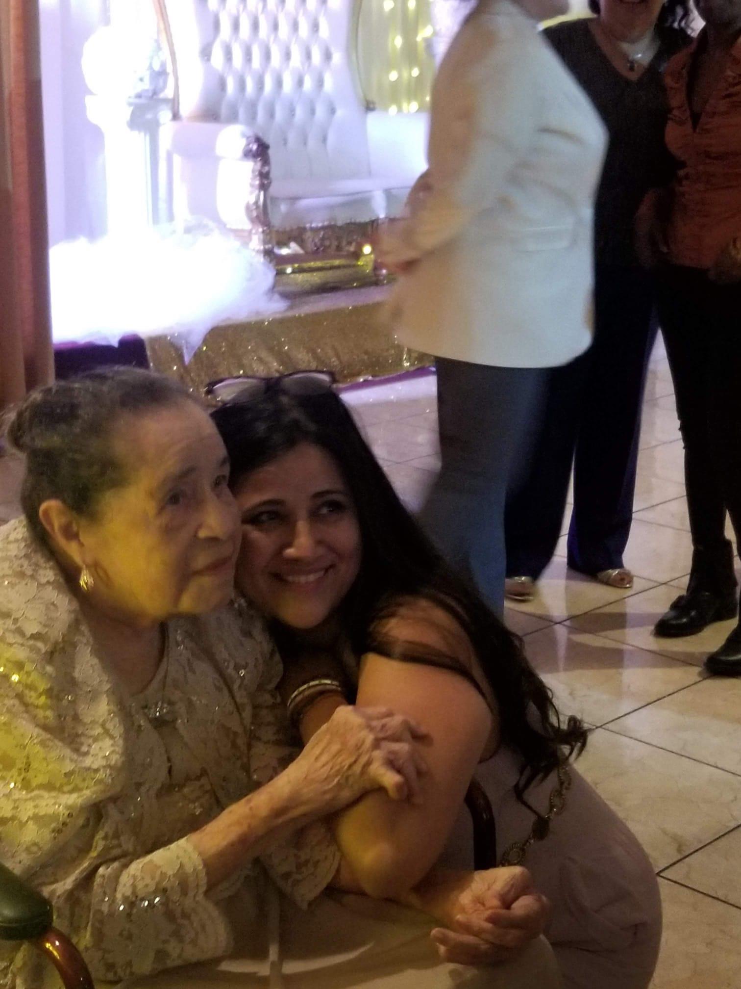 An elderly woman and a younger relative embrace and enjoy a family gathering in a festive setting.