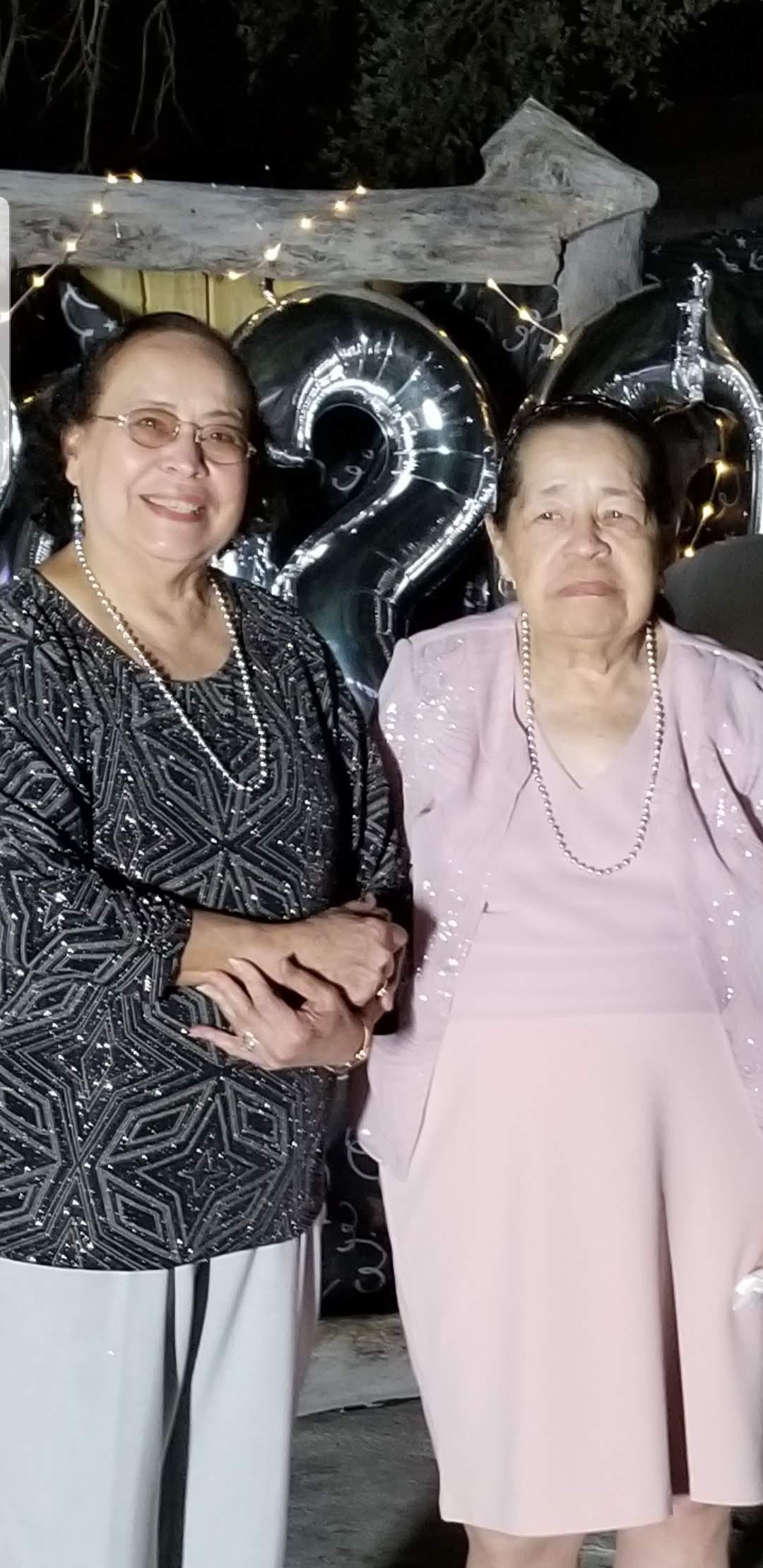 Elderly women smile at a birthday party, surrounded by balloons and decorations.
