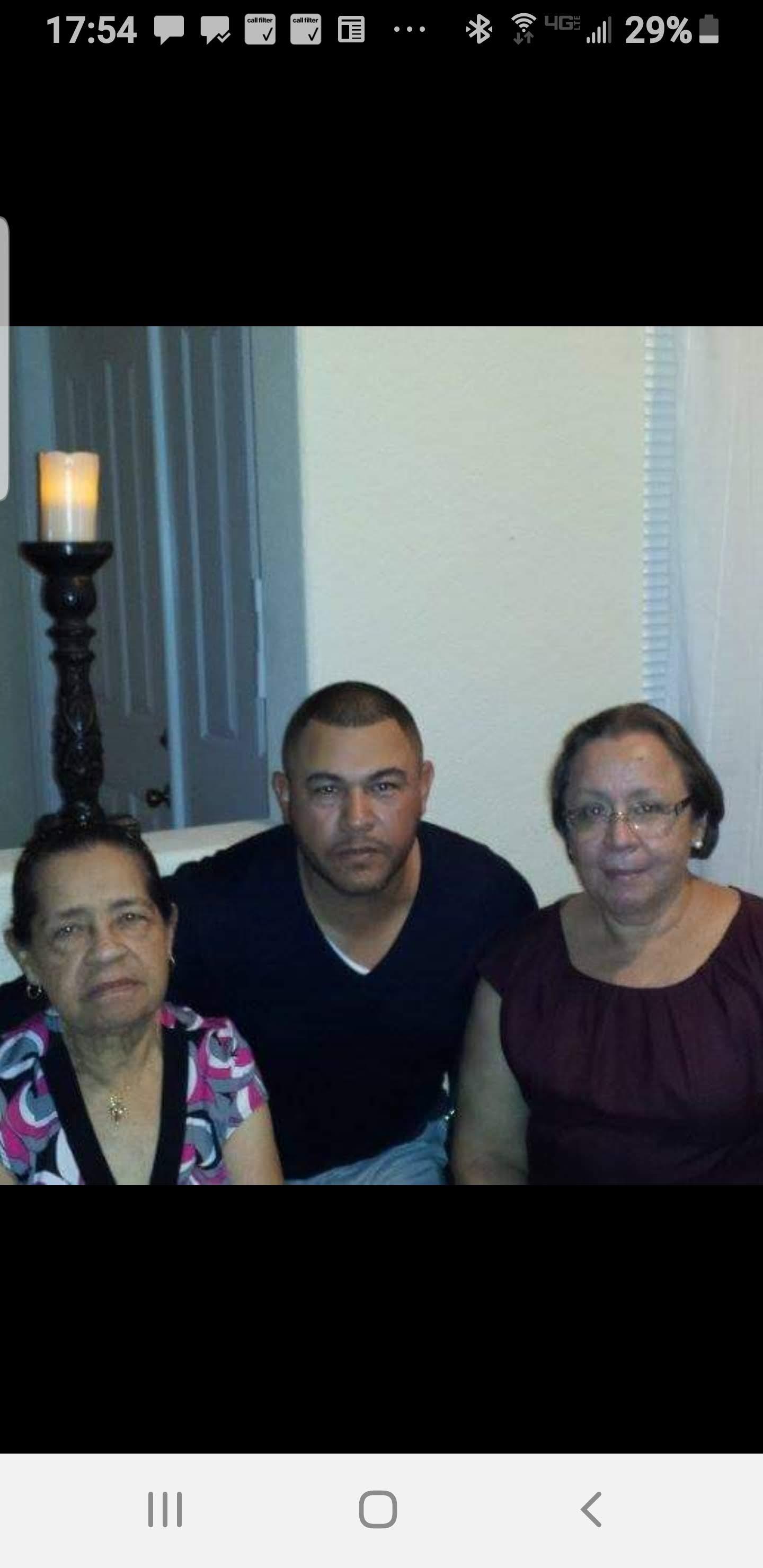 Three family members pose together, smiling warmly in a living room with soft lighting.