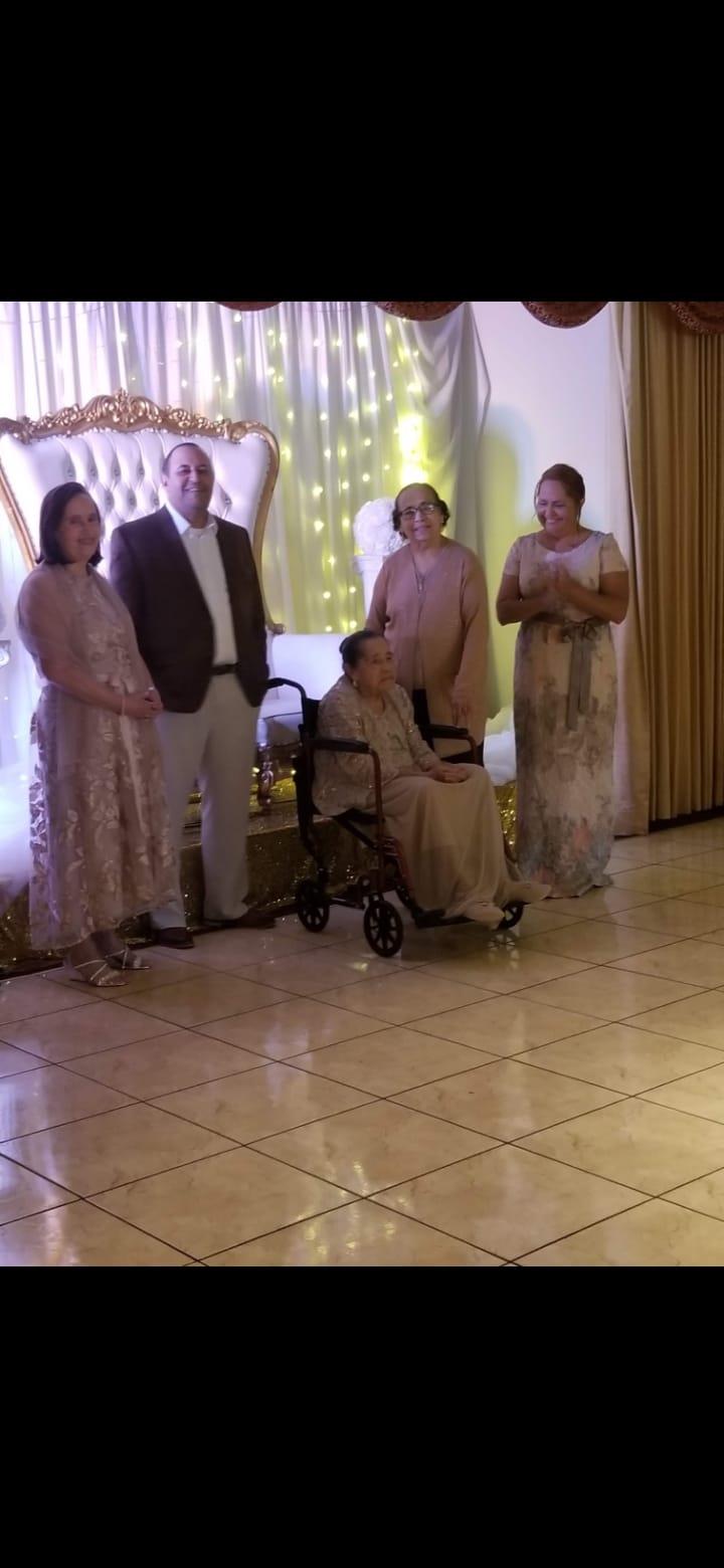 Family gathered around an elderly woman in a wheelchair at an indoor celebration.