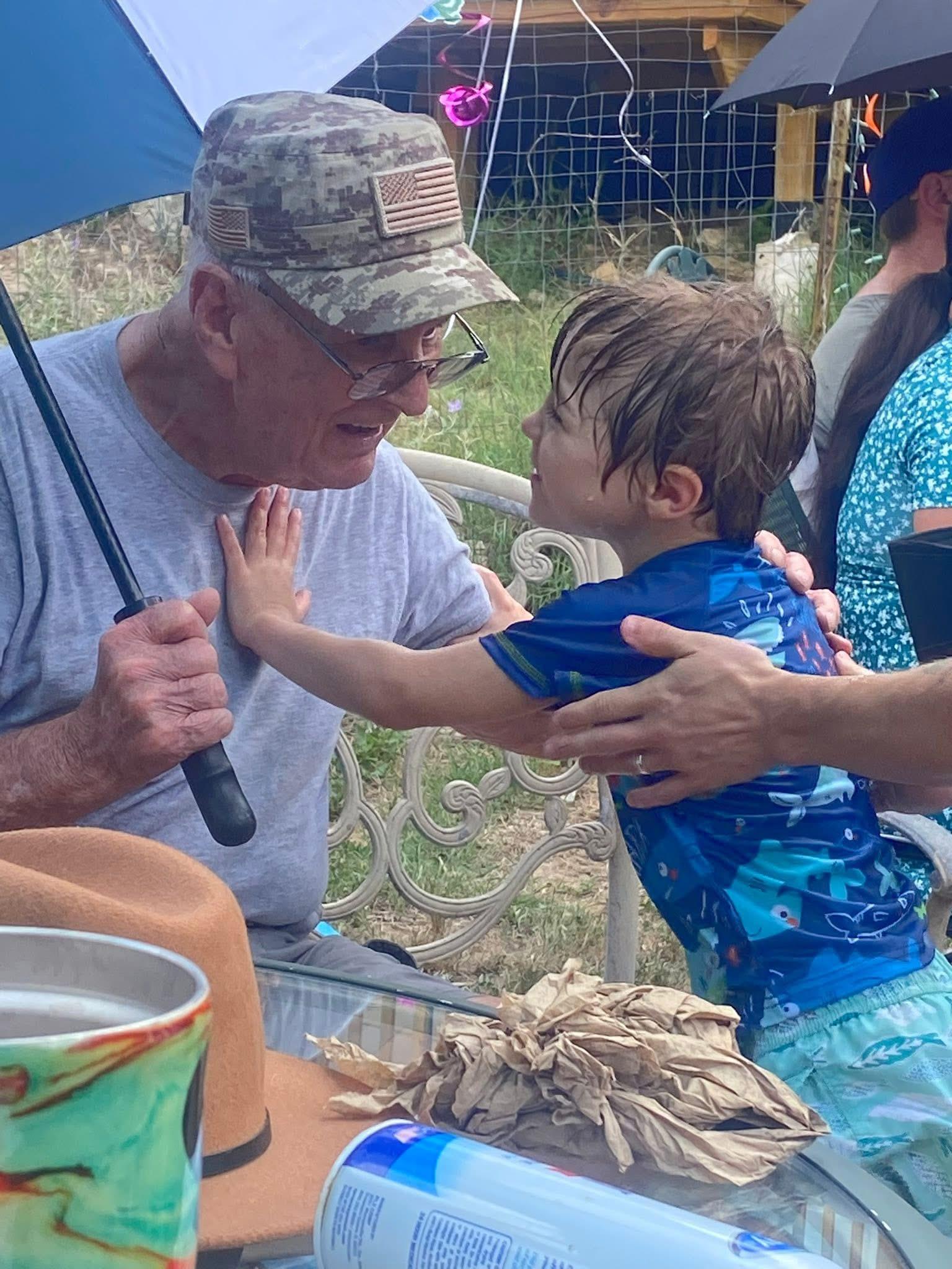 Joyful interaction between a grandfather and his grandson in a backyard, surrounded by family.