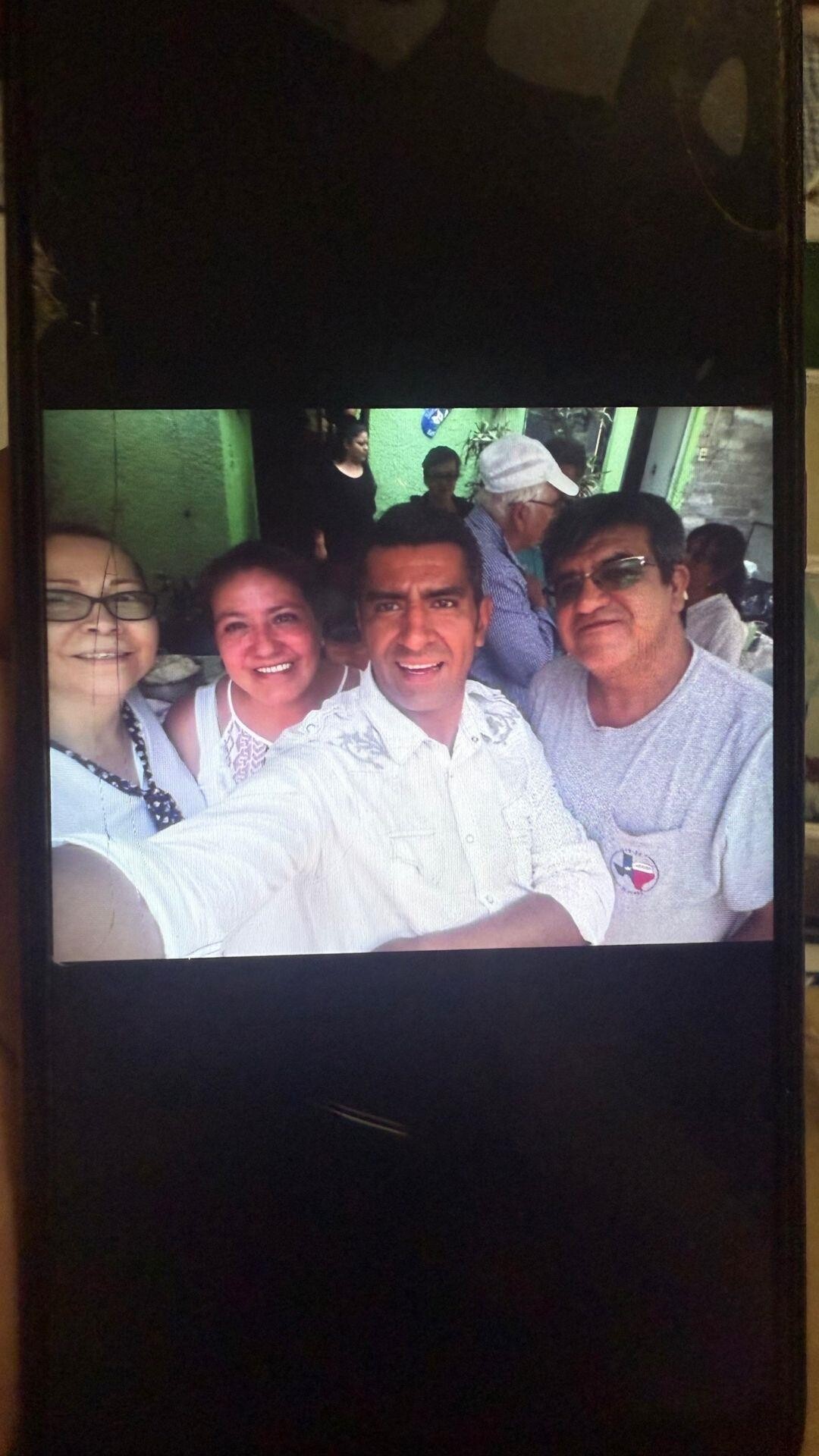 Friends share smiles while taking a selfie at a lively outdoor gathering in the afternoon sun.