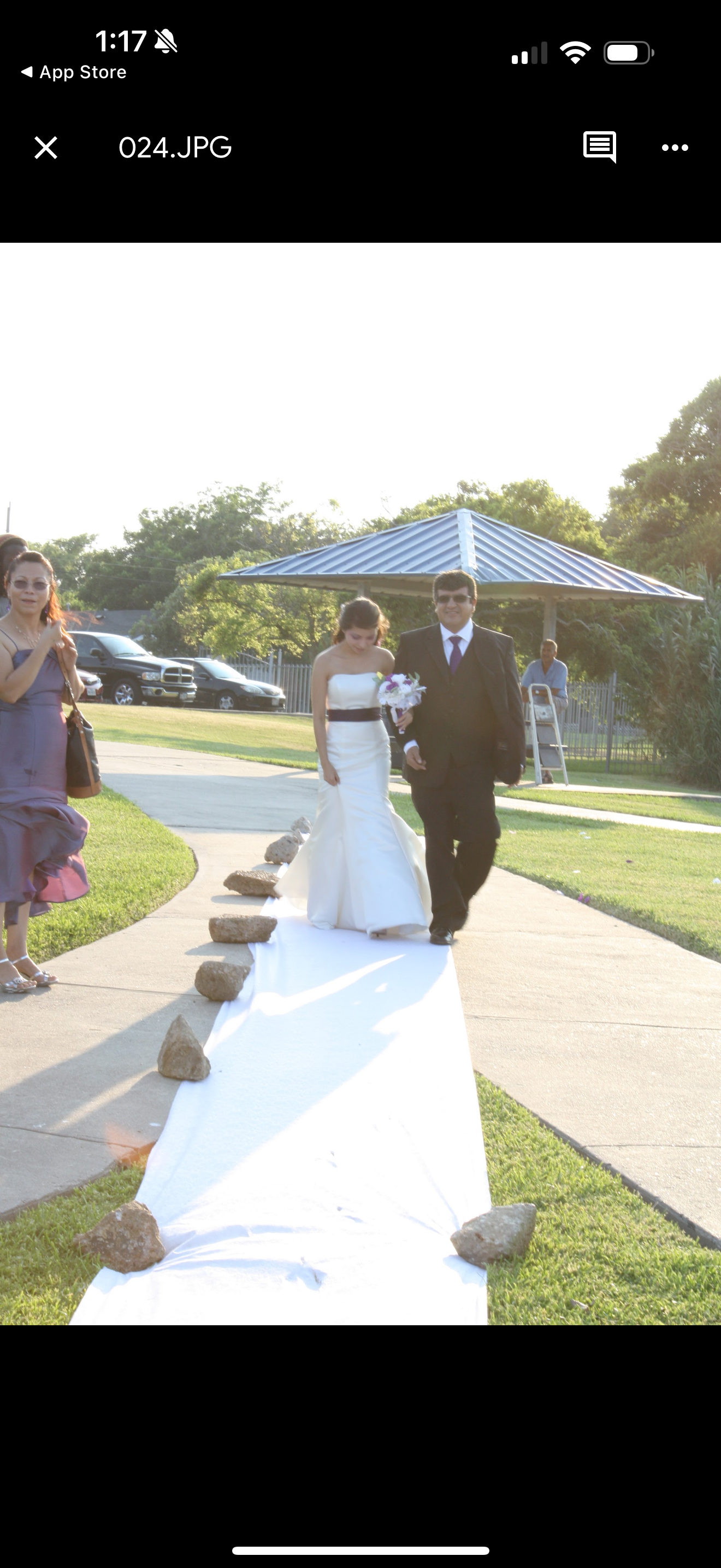 Bride and groom walk along a white carpet with guests watching at a wedding ceremony.