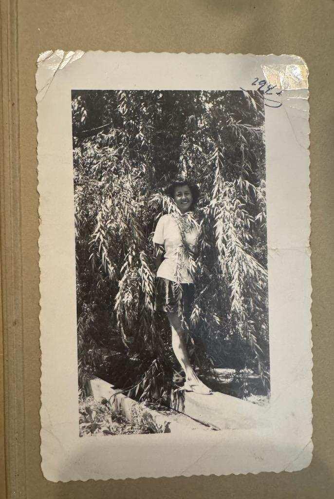 A young woman stands playfully next to a willow tree, enjoying a sunny day outdoors.