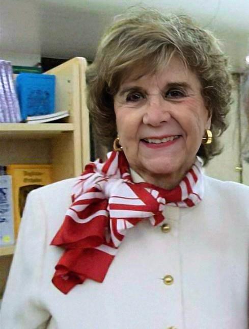 A cheerful elderly woman poses with a friendly smile in a warm indoor environment.