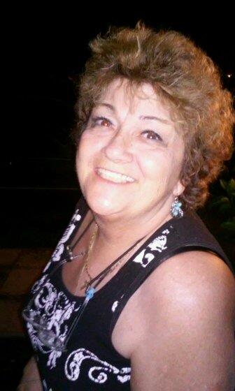 A joyful woman with curly hair smiles brightly during an outdoor event at night.