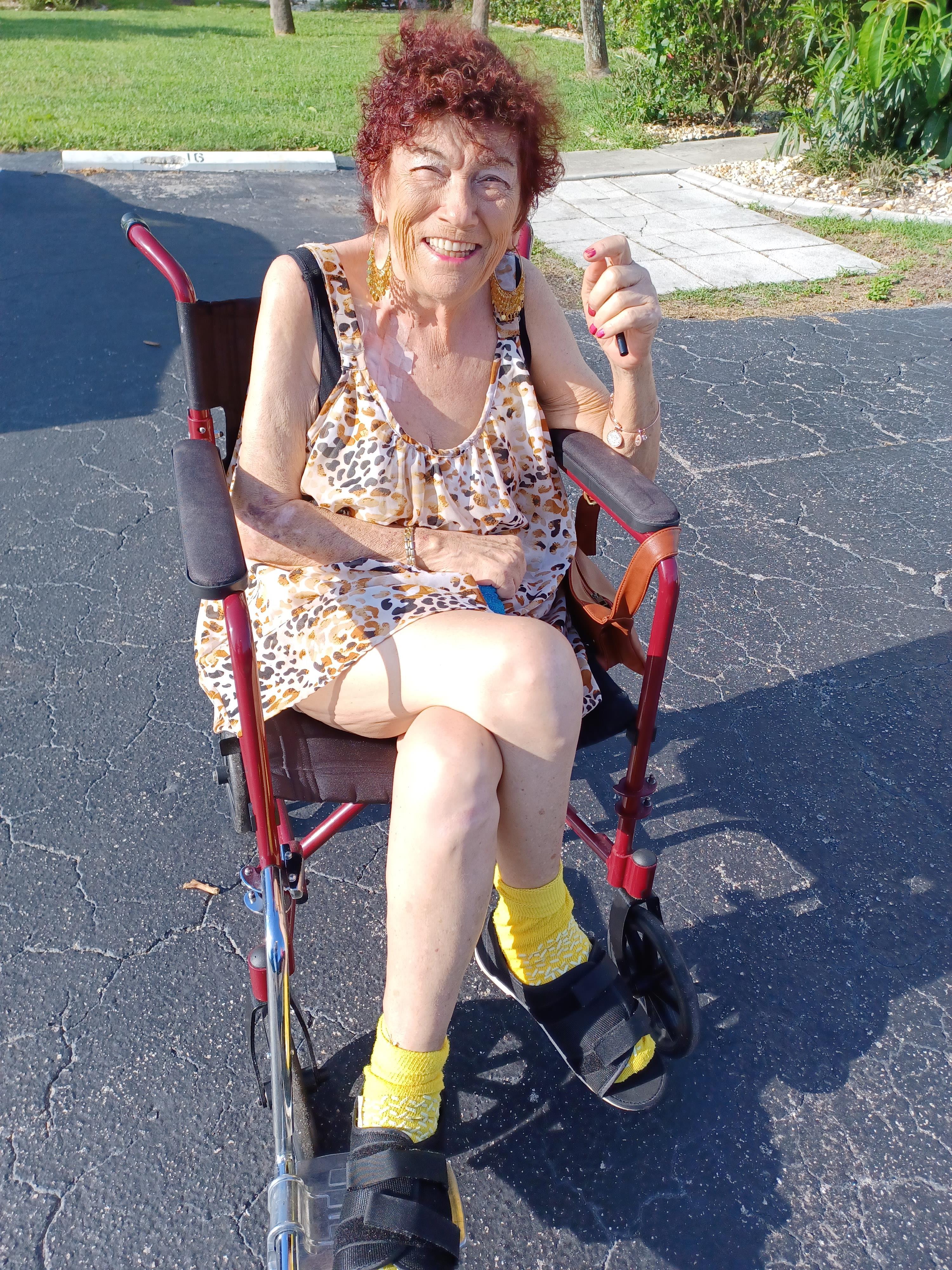 An elderly woman enjoys the sun in a colorful outfit while sitting comfortably in her wheelchair.