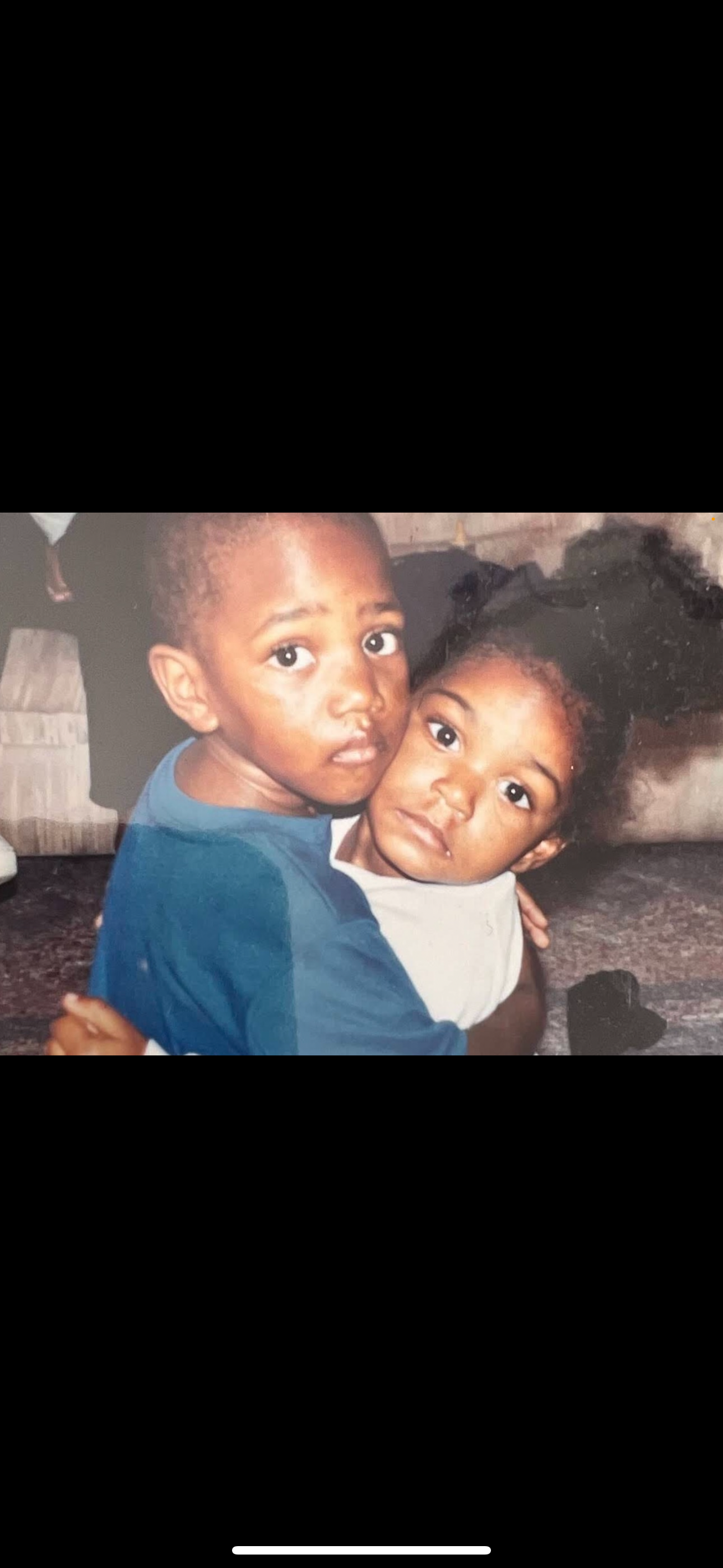 Two young children hold each other closely, showing affection in a warm indoor space.