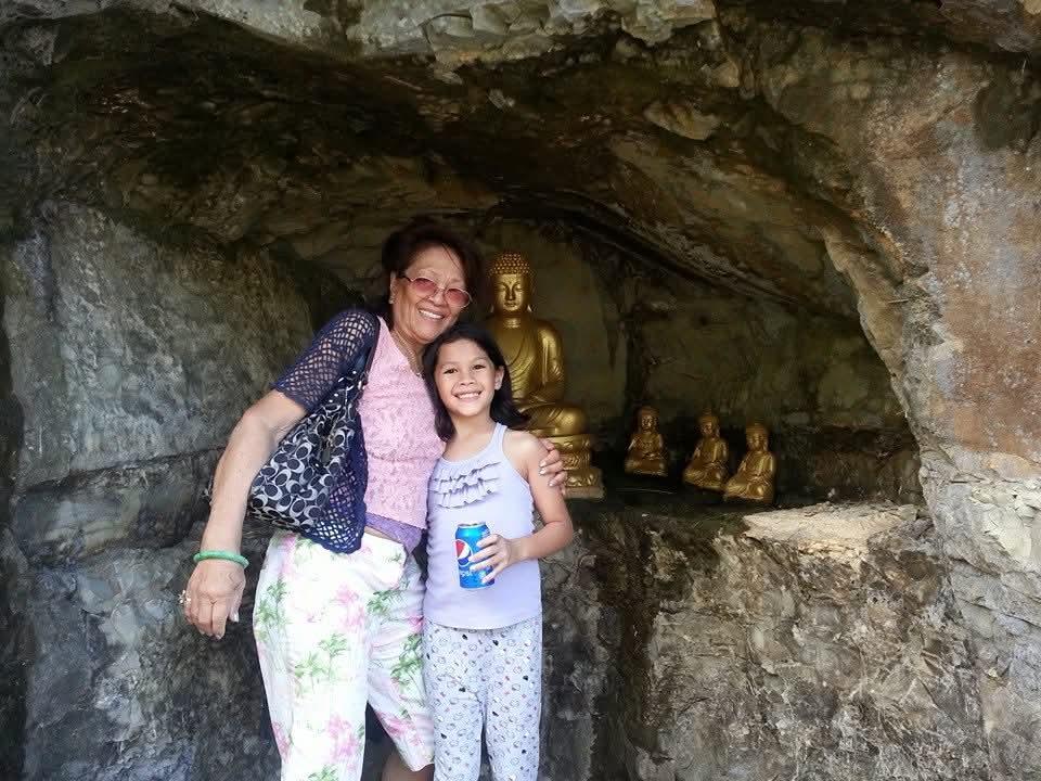 Grandmother and granddaughter share a joyful moment in a cave with golden statues behind them.