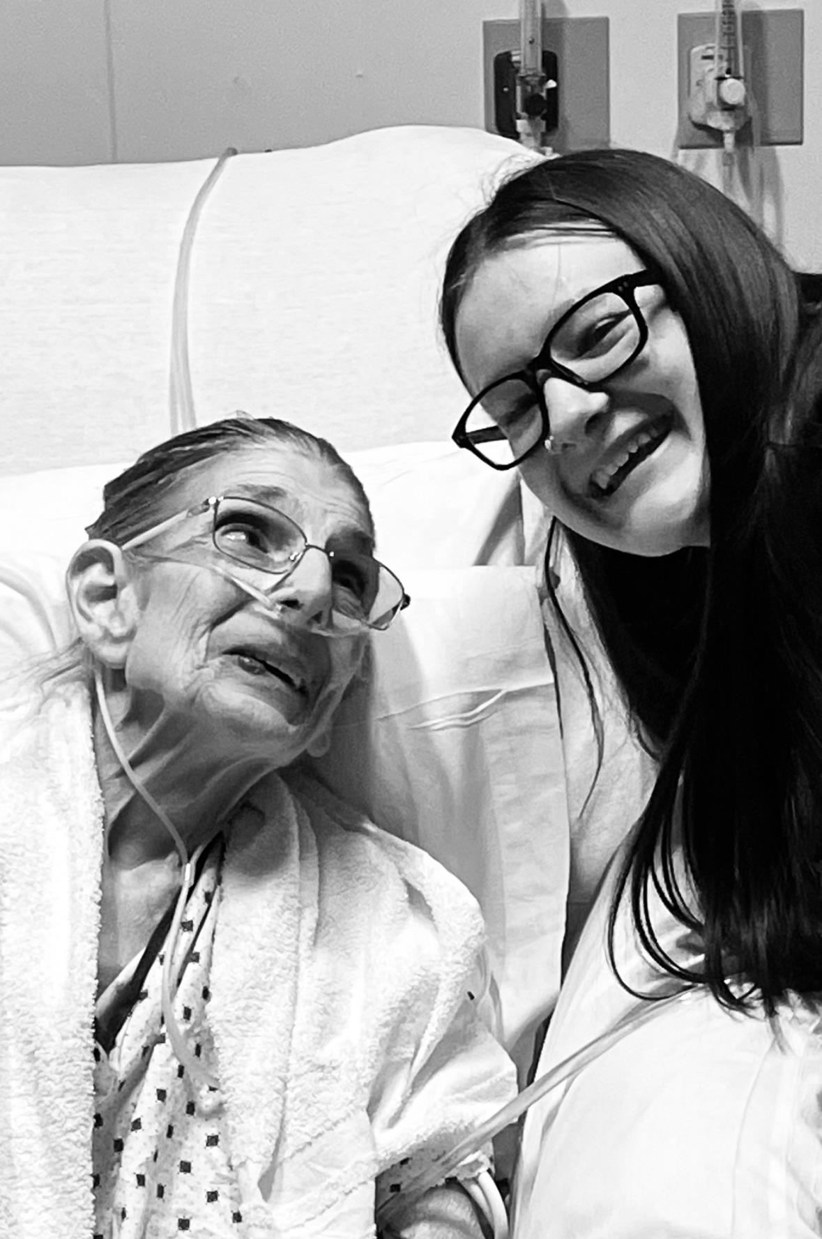 A woman shares a joyful moment with her elderly relative in a hospital bed, both smiling warmly.