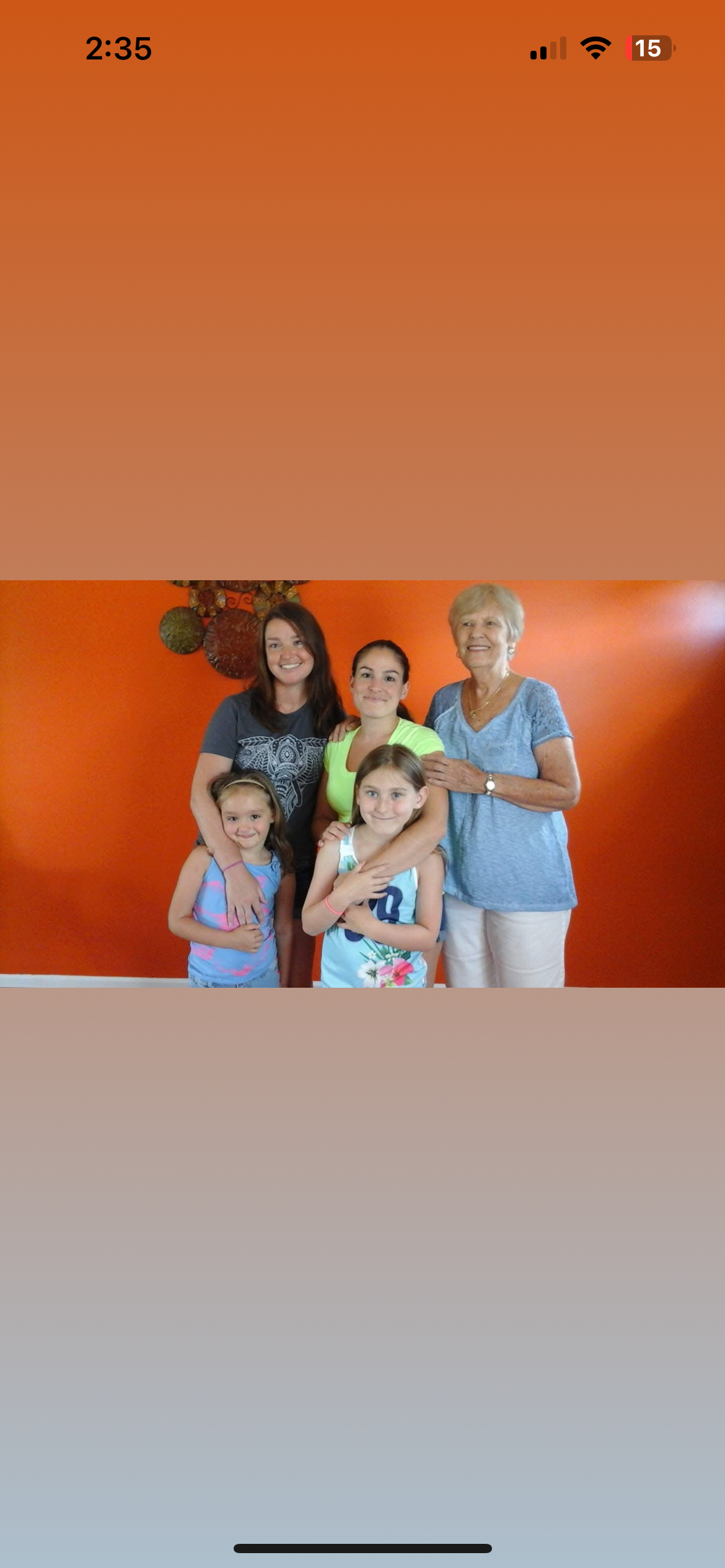 Five family members smile together against a bright orange backdrop, radiating joy.