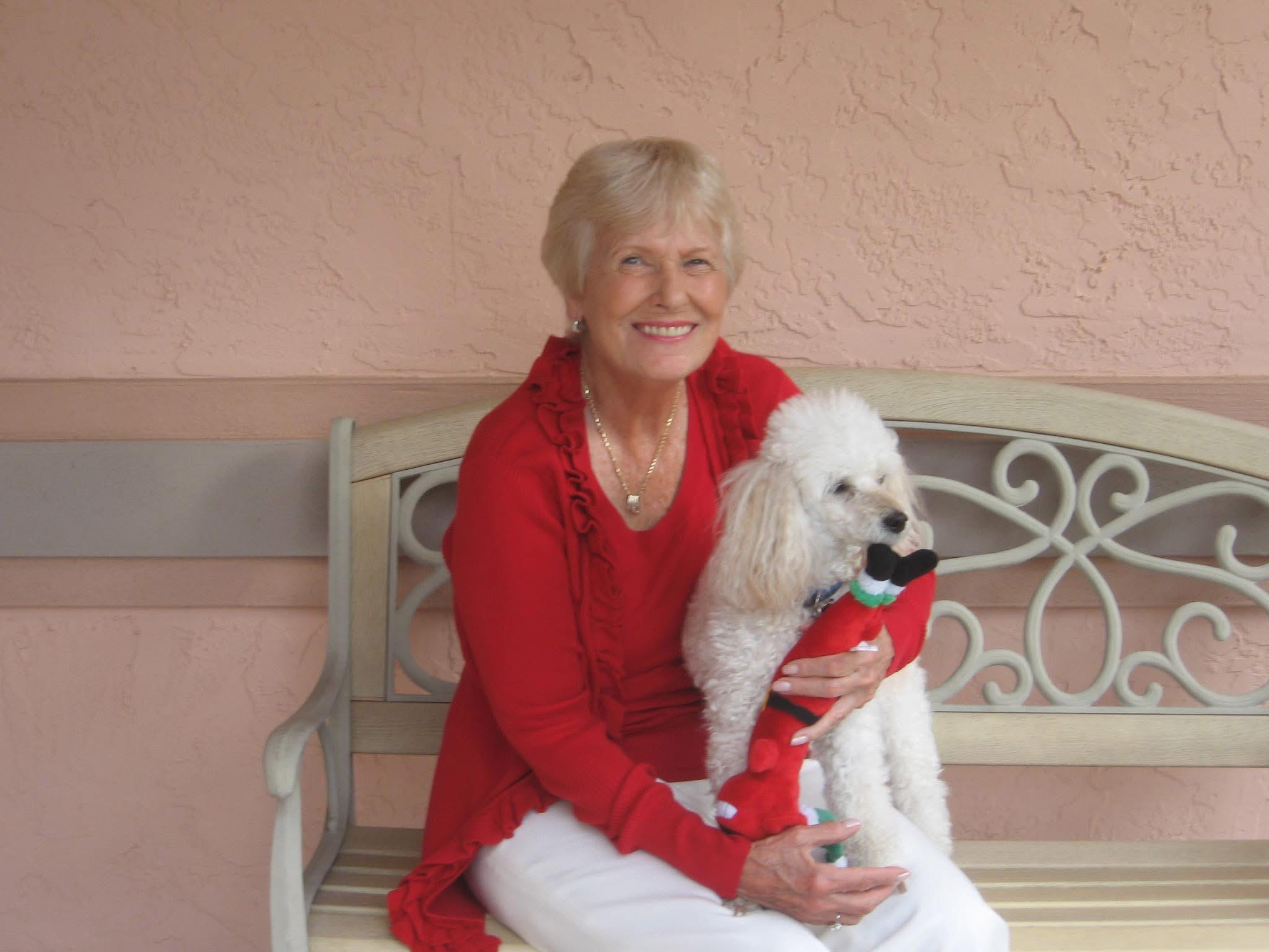 Senior woman joyfully embraces her small white dog while sitting on a bench outside.
