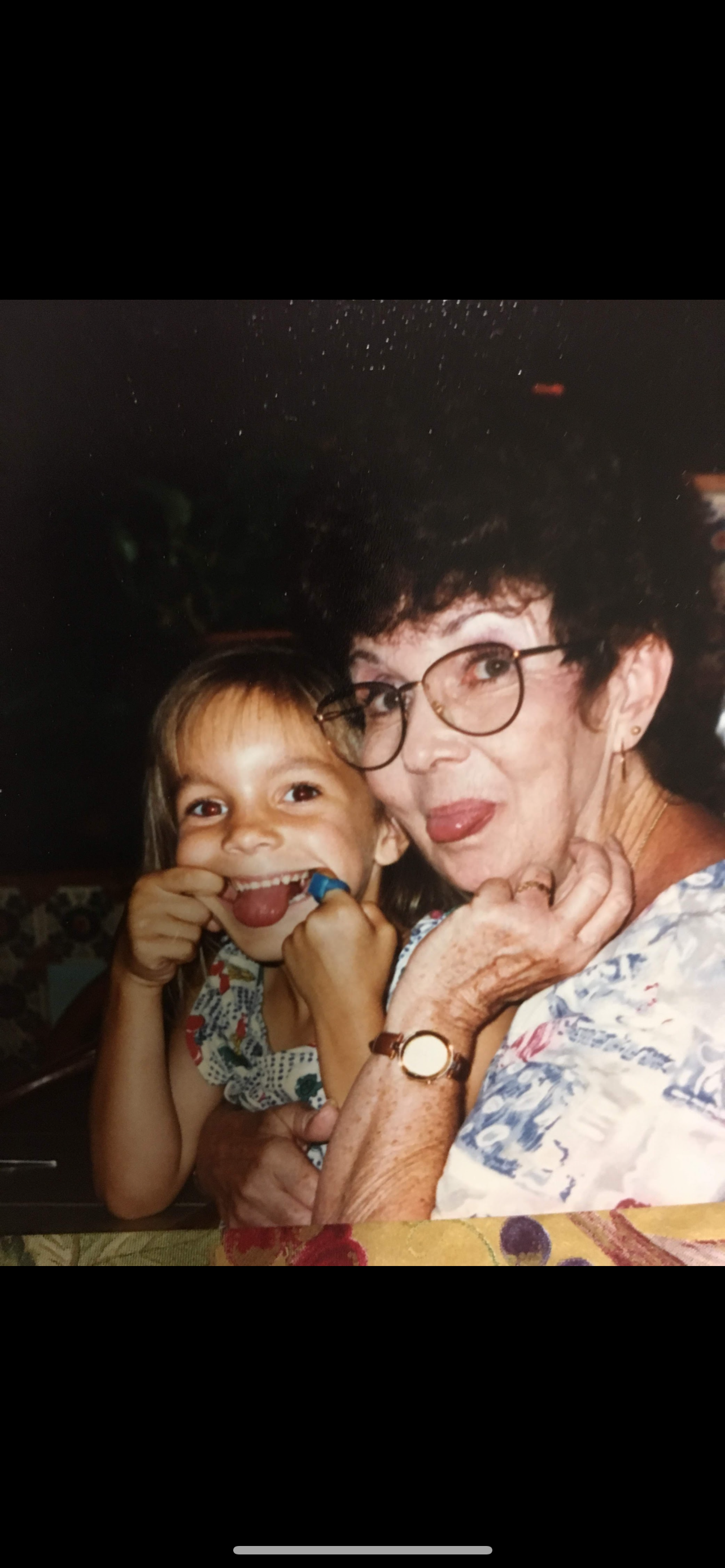 A girl and her grandmother smile playfully together at a family gathering.