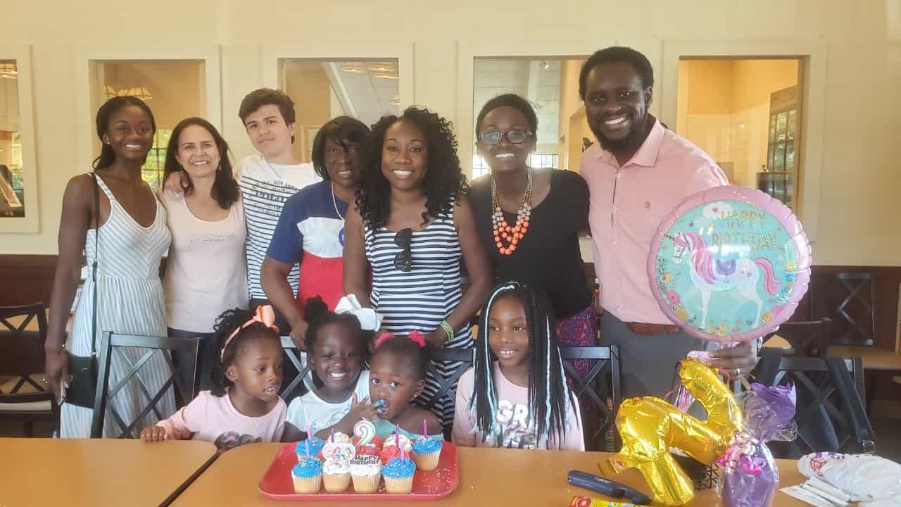 Family and friends joyfully celebrate a birthday at a restaurant with cupcakes and balloons.