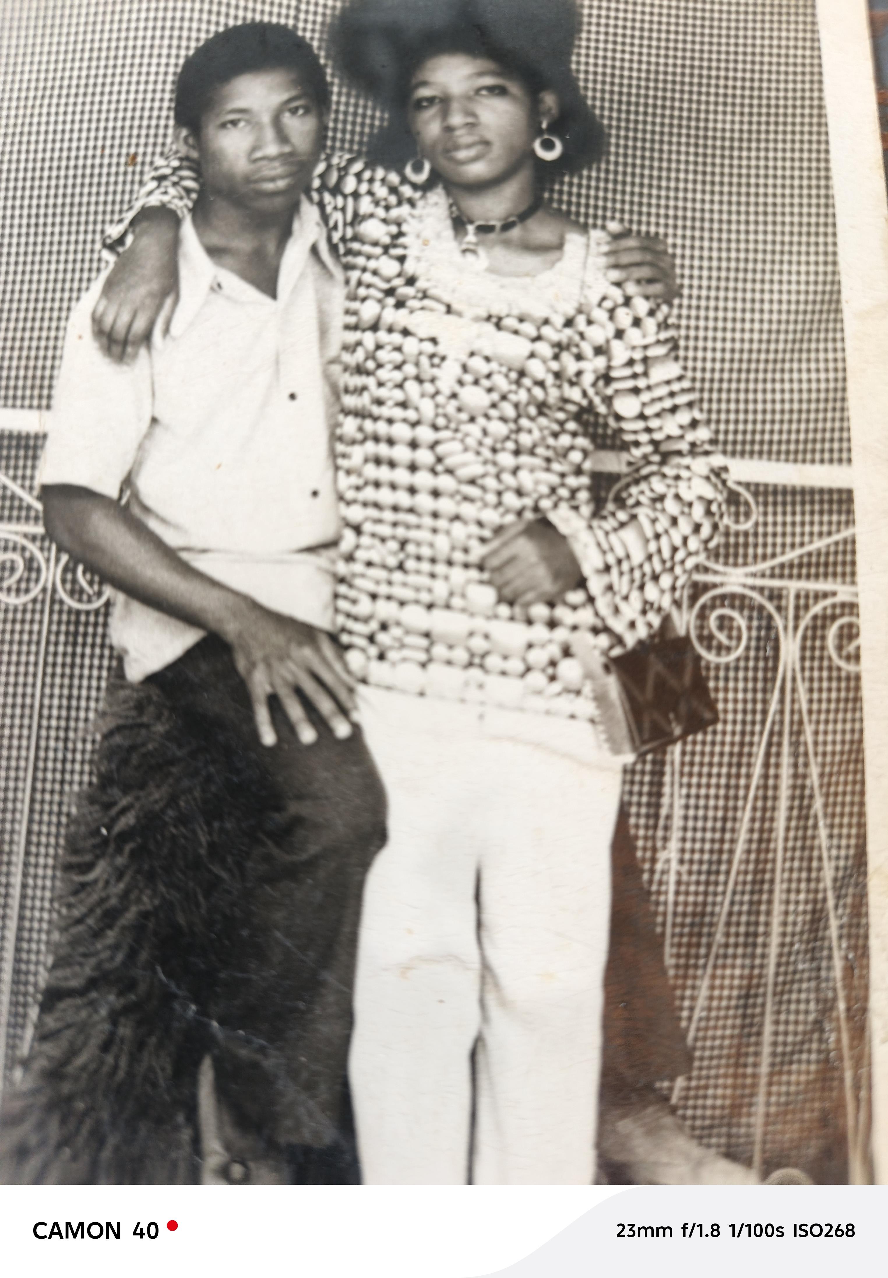 Two individuals stand close, smiling while wearing colorful traditional clothing.