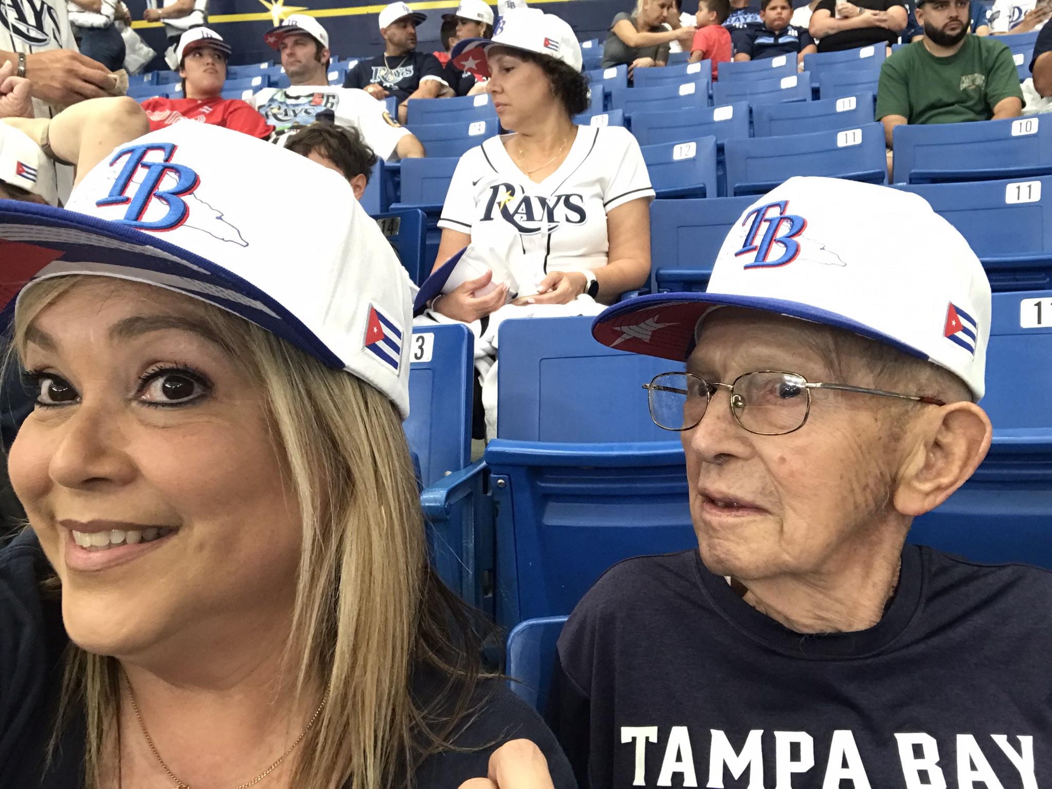 Two fans capture a selfie while enjoying a lively baseball game in their team hats.