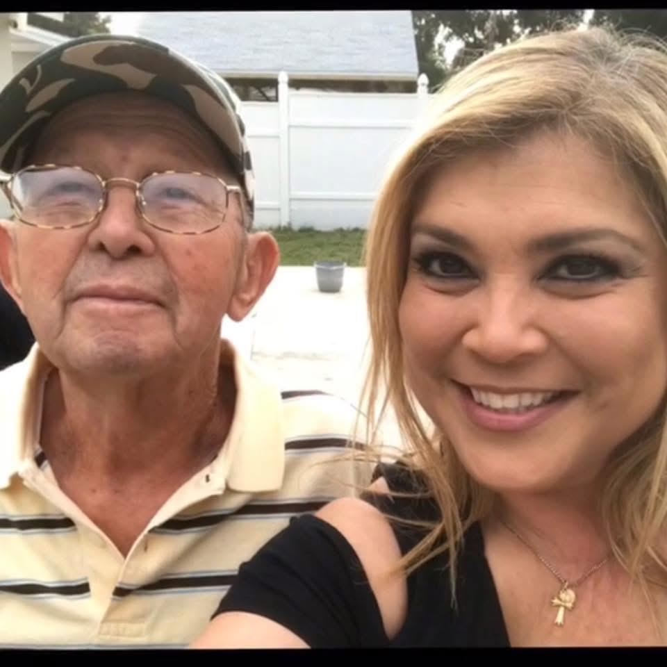 Two family members smile and pose for a selfie in a garden during daylight hours.