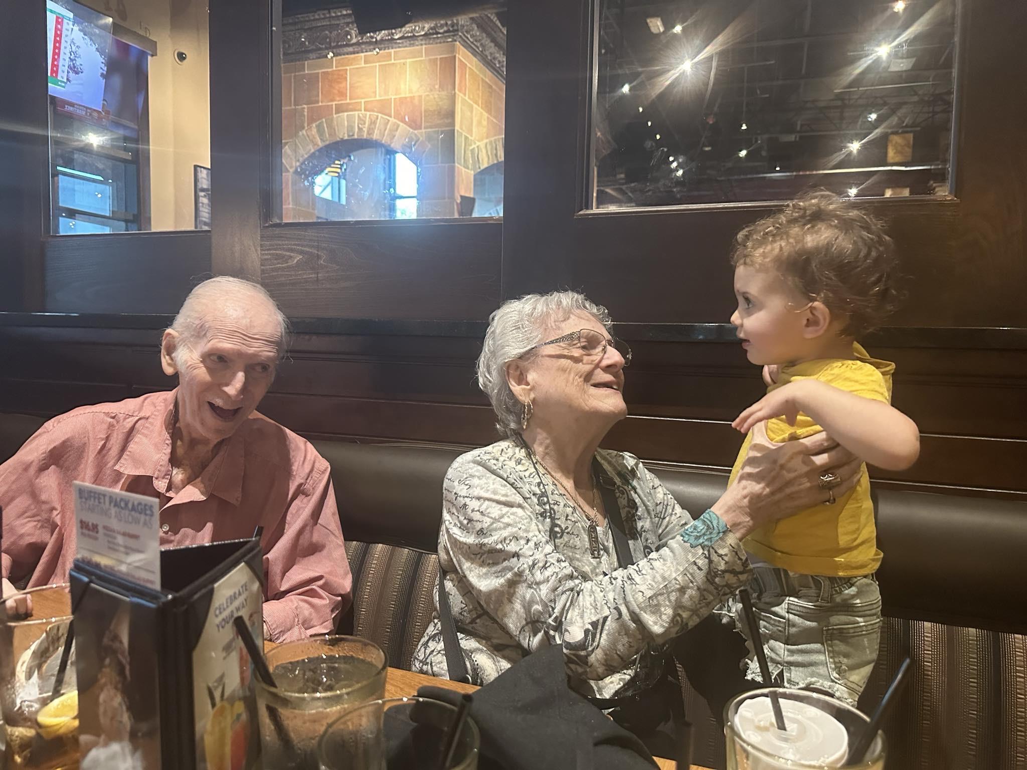 Grandparents delight in playful interaction with their young grandchild during dinner.