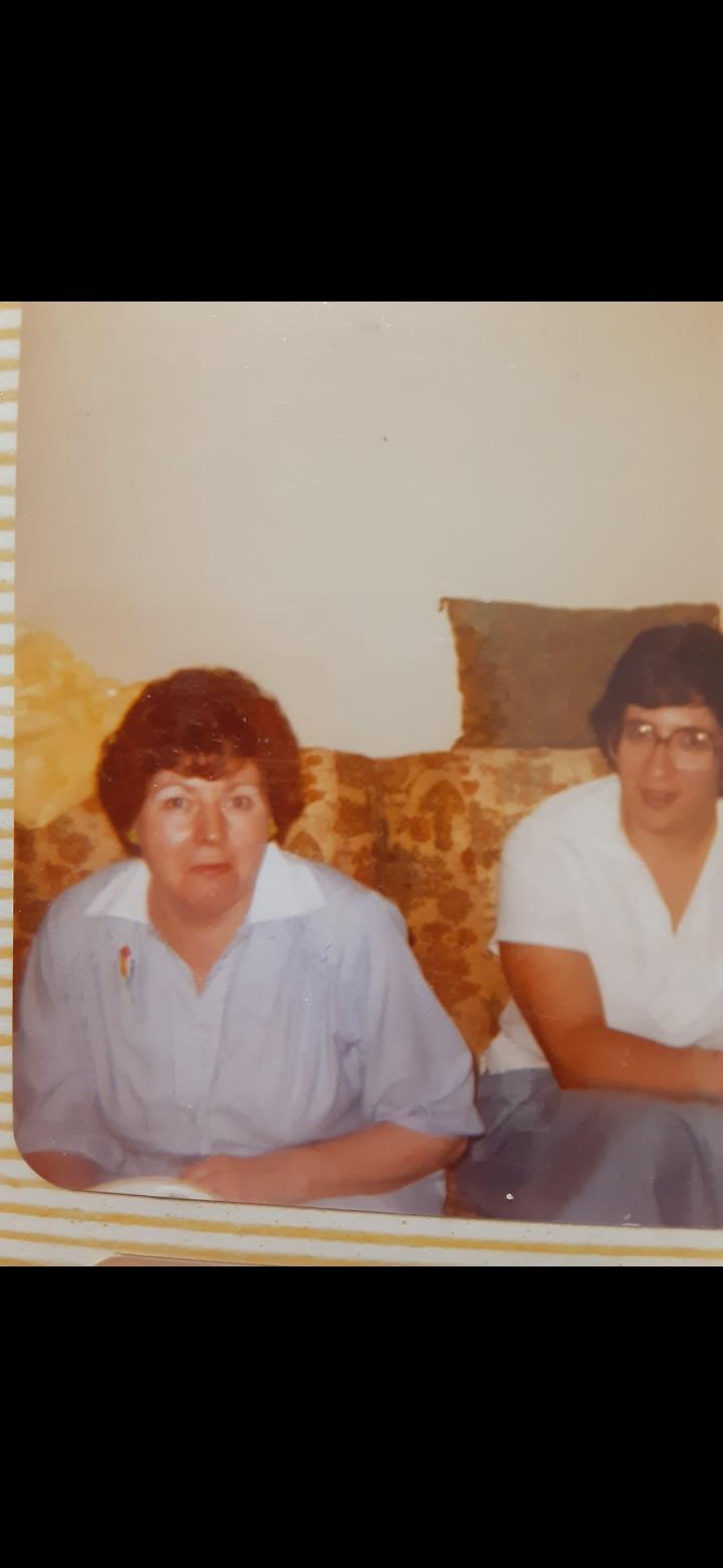 Two women relax on a patterned couch, sharing stories in a vintage living room setting.