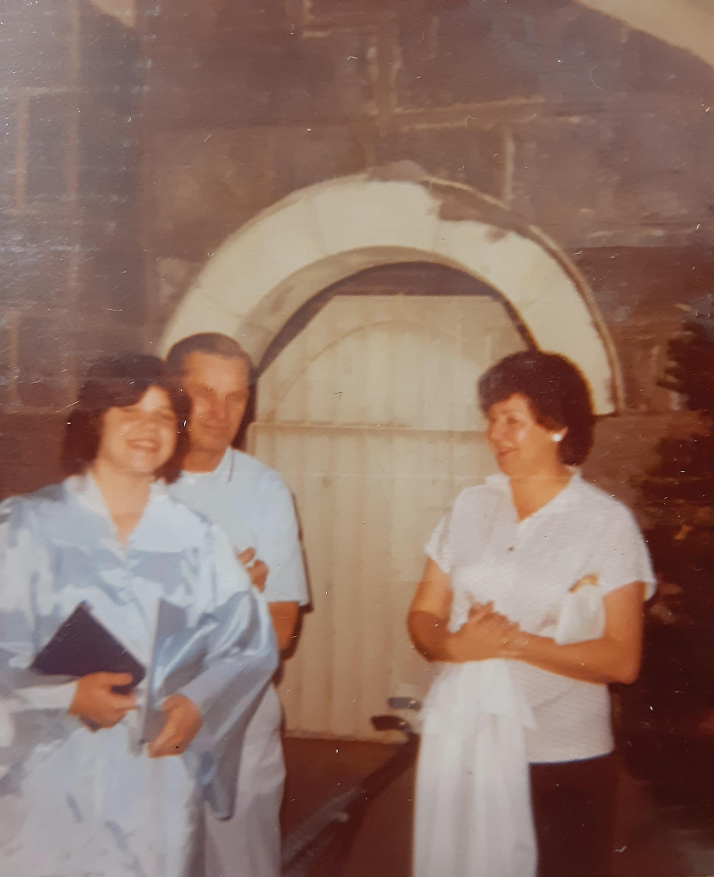 Three people are enjoying a special moment outdoors next to a historic stone arch.